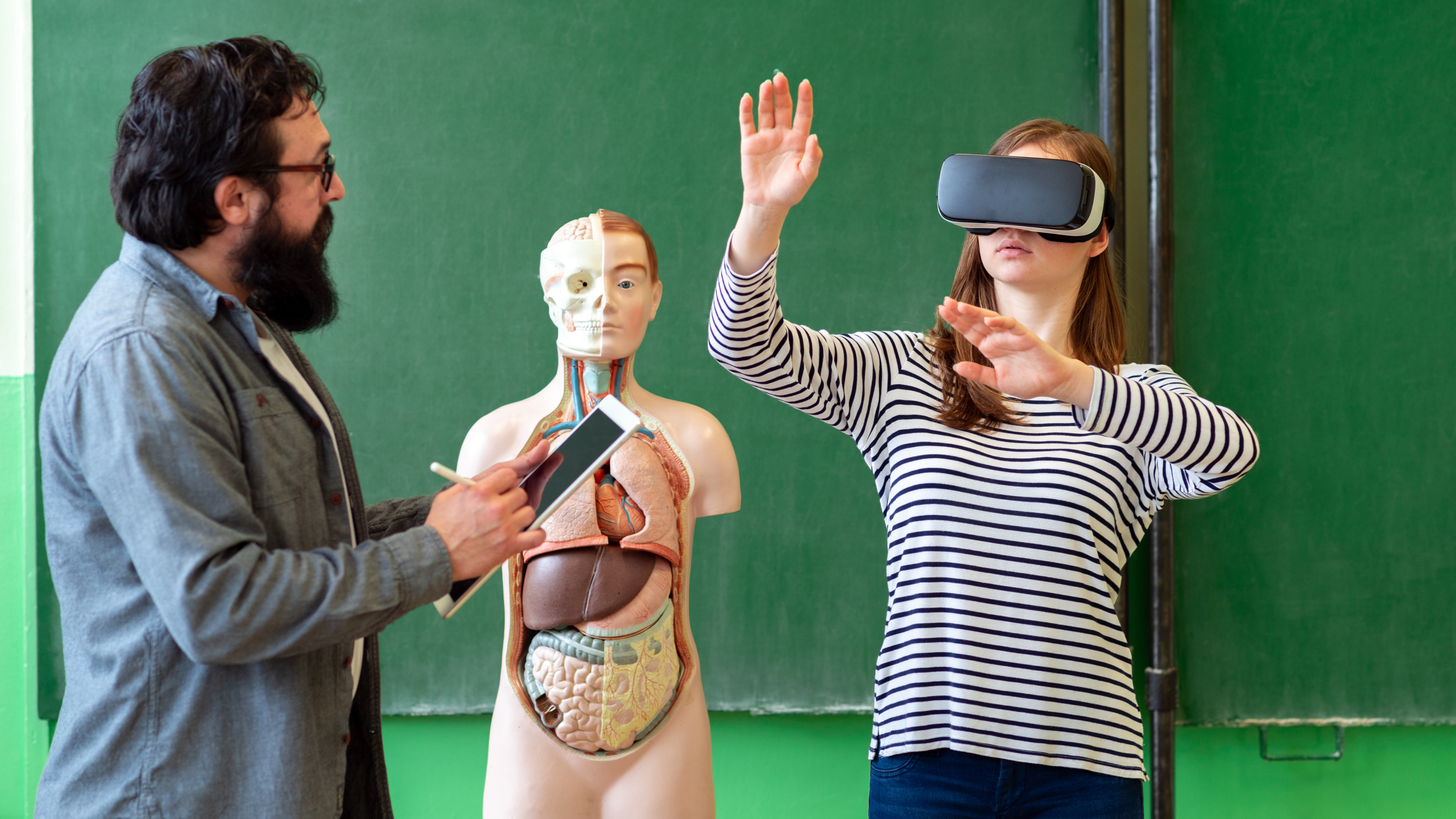 Young teacher using Virtual Reality Glasses and 3D presentation to teach students in biology class. Education, VR, Tutoring, New Technologies and Teaching Methods concept.