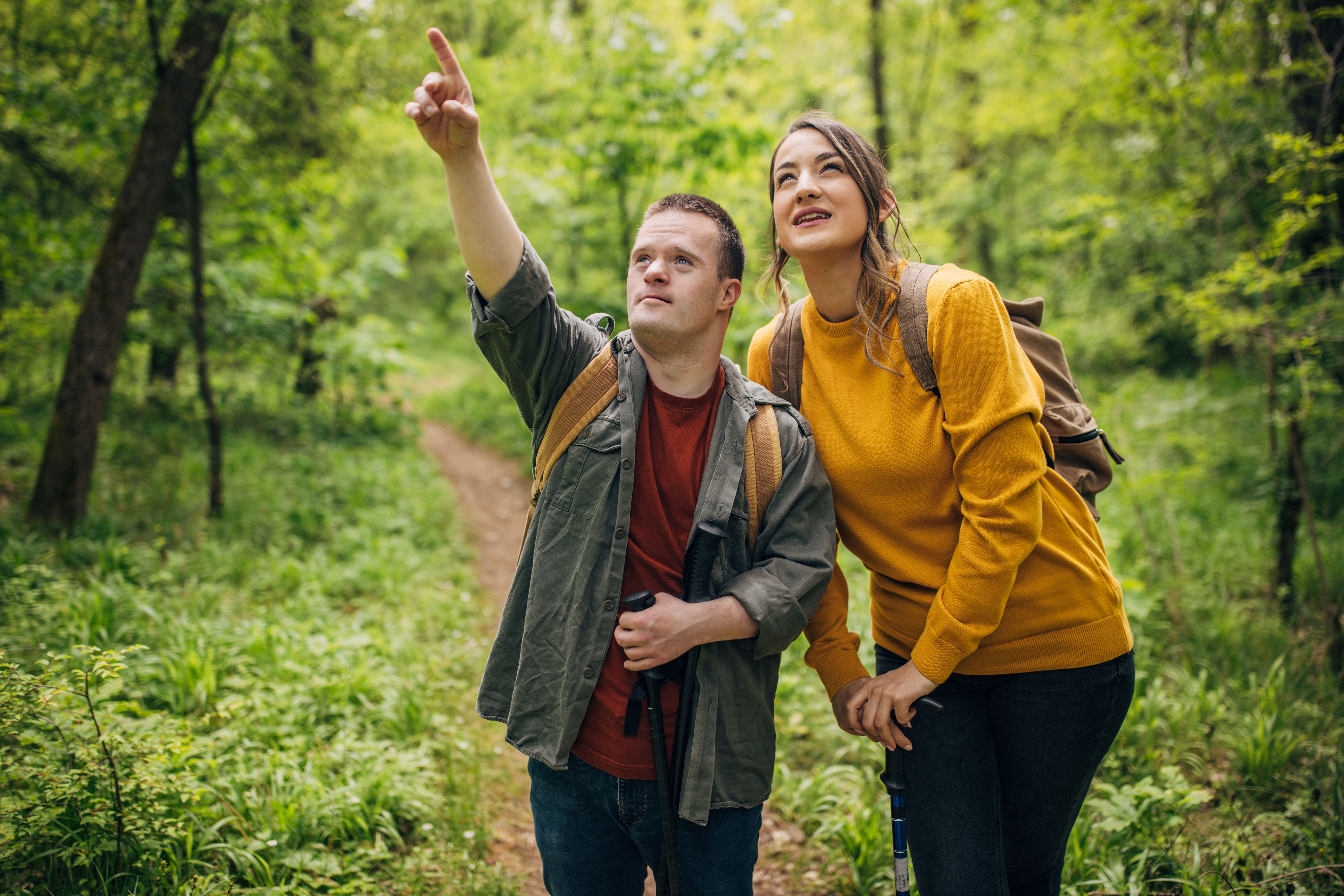 Two friends, a young woman and man with Down syndrom, hiking together in the forest