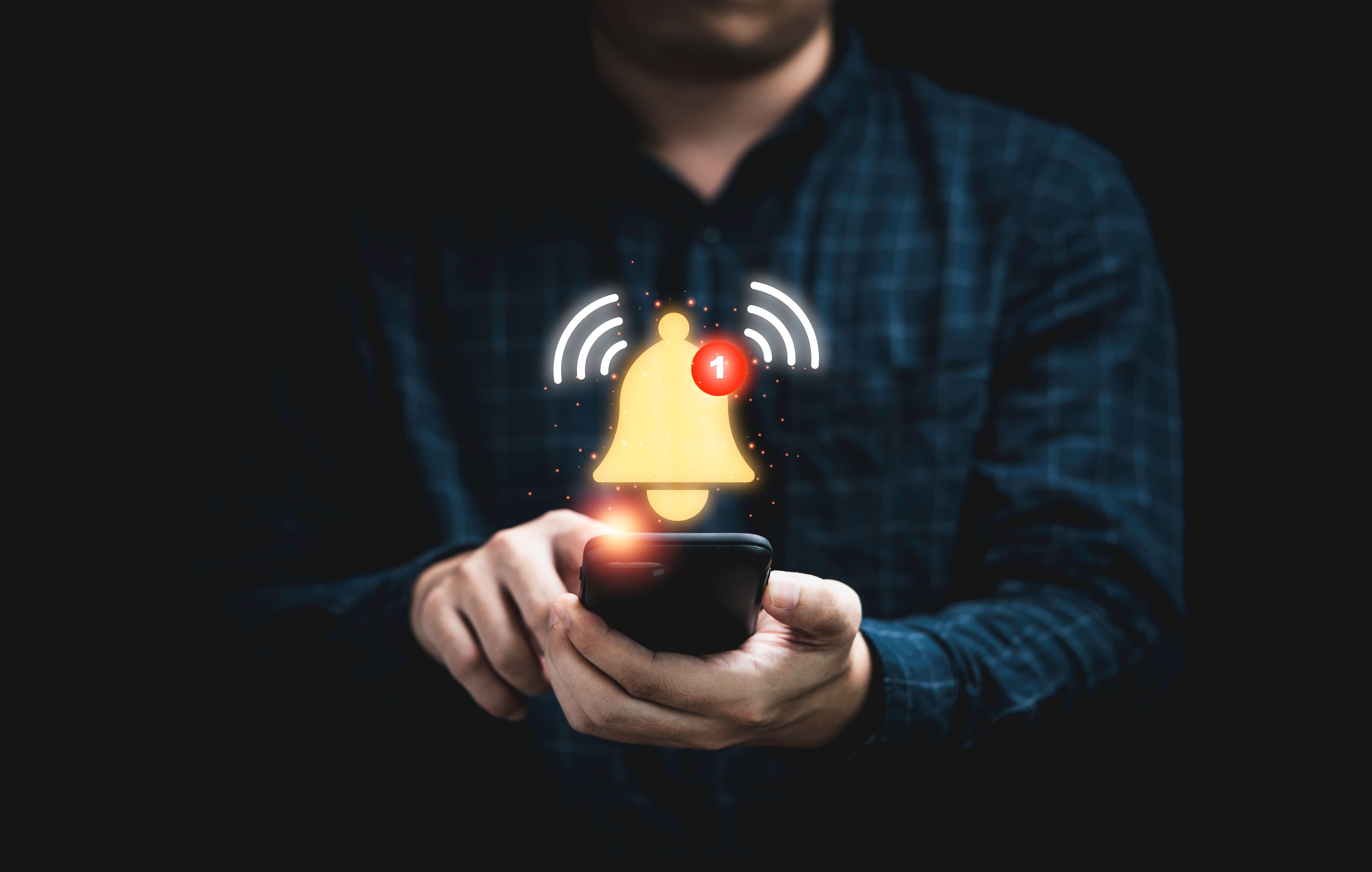 Businessman holding smartphone with virtual yellow bell ringing for application notification alert concept.