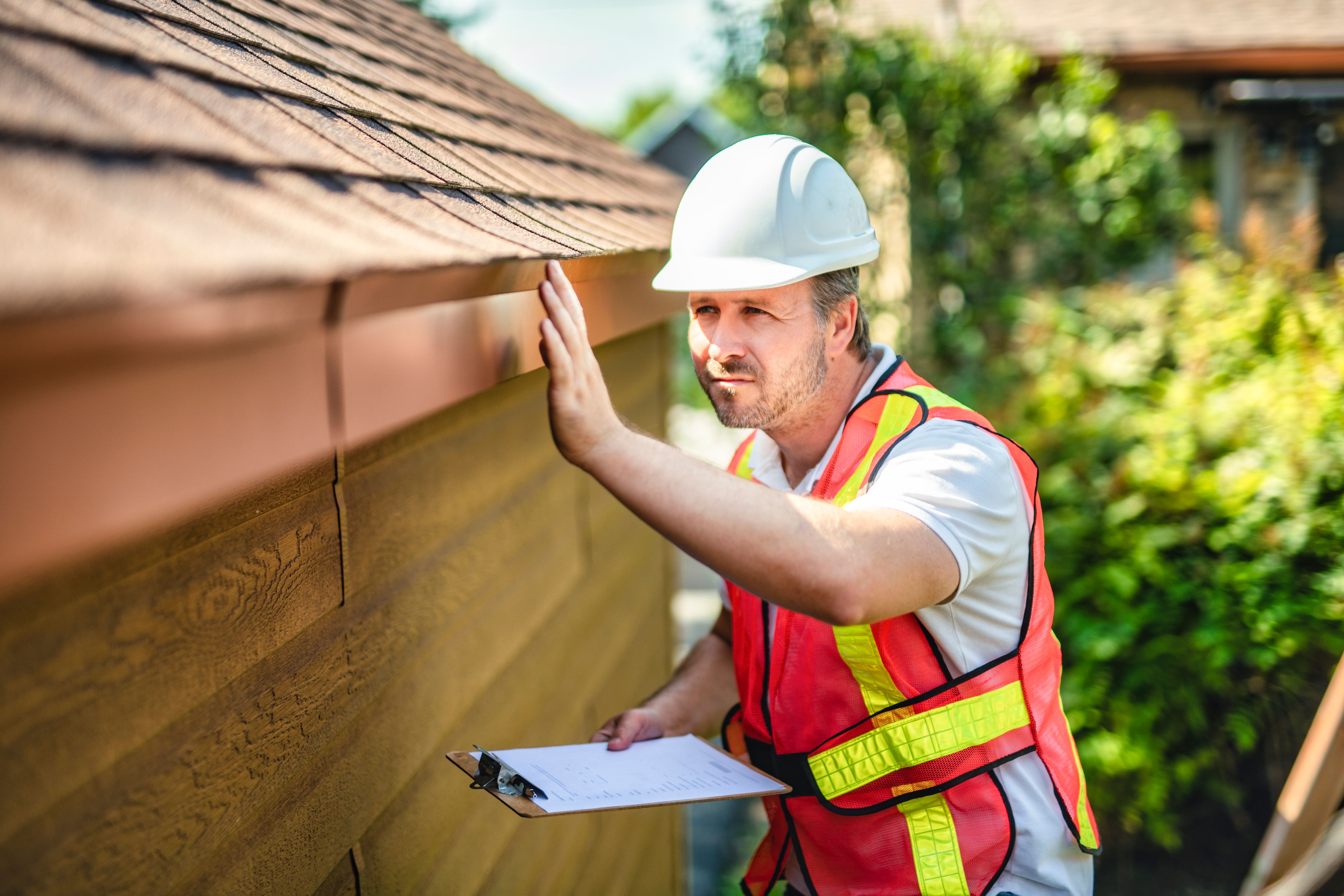 man with hard hat standing on steps inspecting house roof