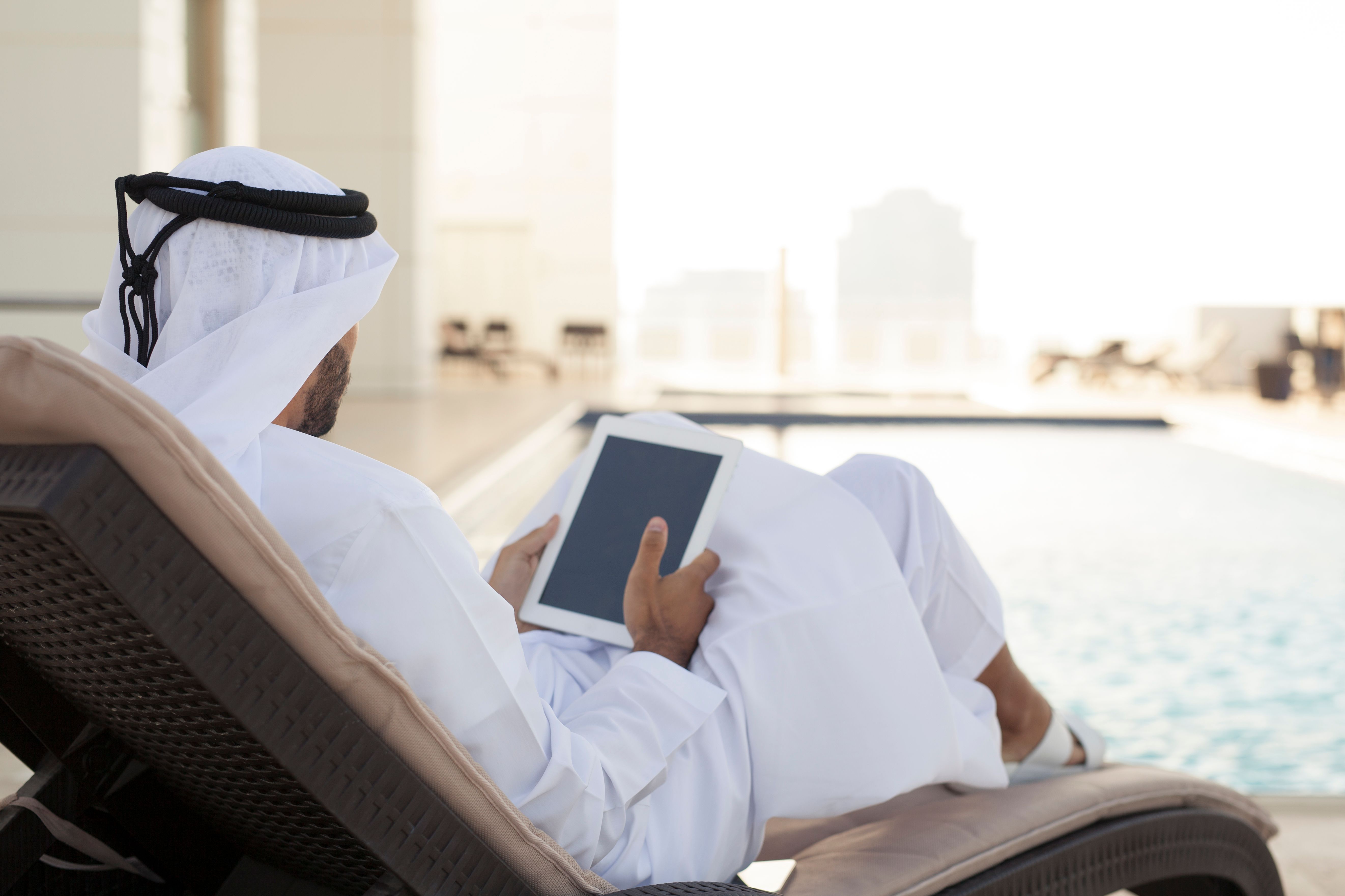 Arab Man Using Digital Tablet Relaxing by Swimming Pool Arab Man Using Digital Tablet Relaxing by Swimming Pool