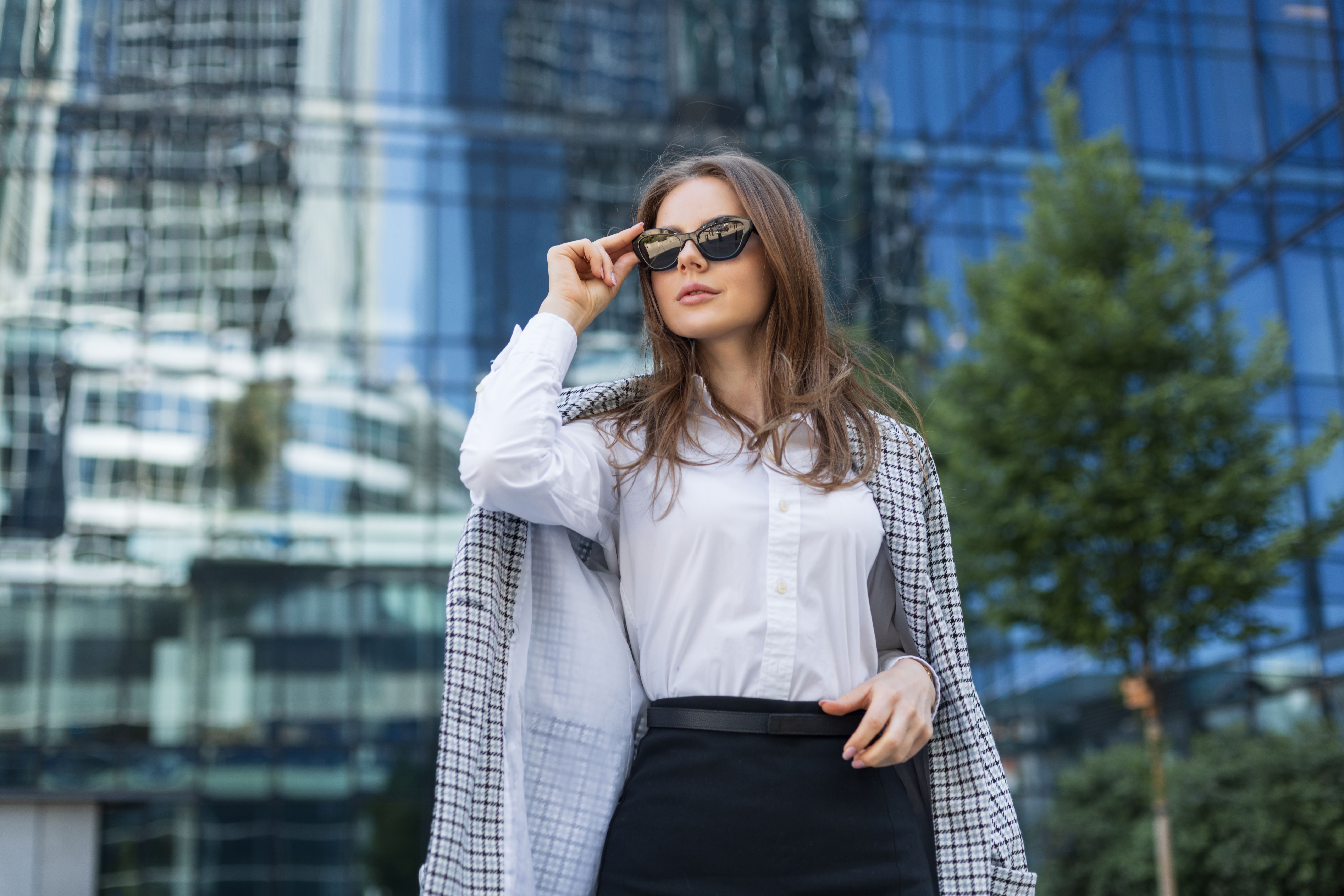 Stylish woman in sunglasses posing confidently in urban environment. Modern business attire and city lifestyle concept.