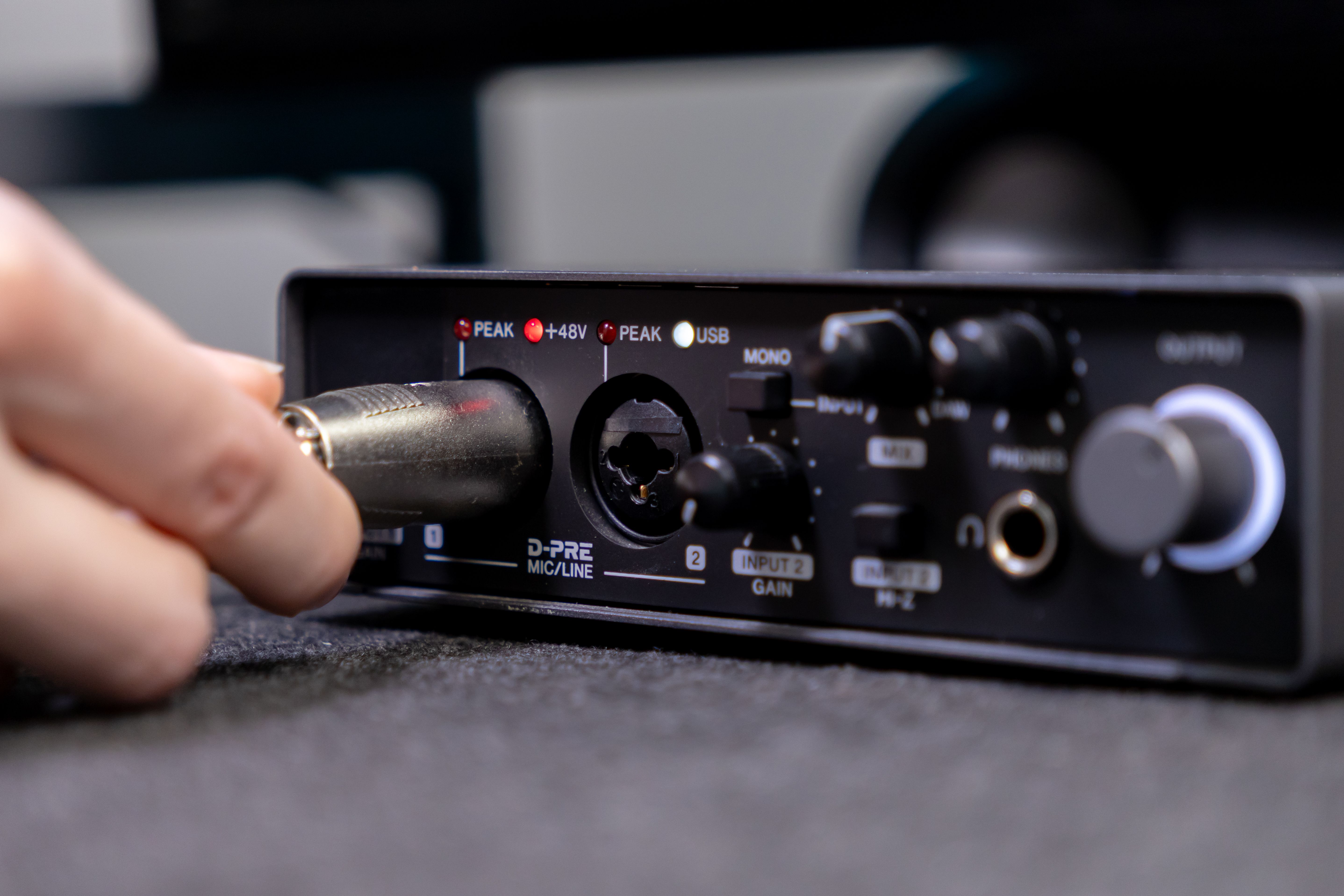 A hand expertly connects an XLR audio cable into the D-PRE MICLINE input of a compact black sound interface, demonstrating professional setup for high-fidelity recording or live streaming