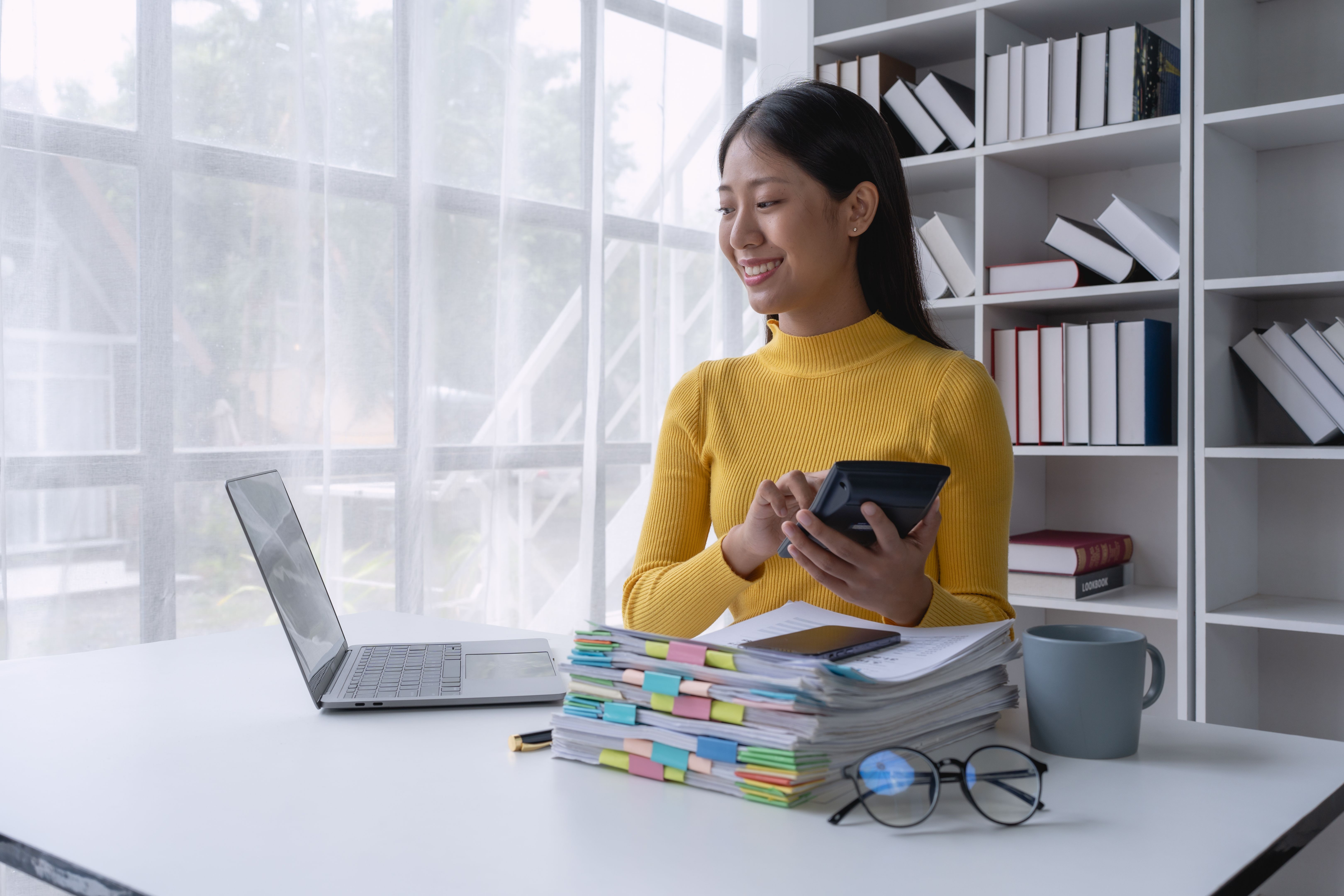 woman meticulously plans a finance audit, using a computer and calculator to review budget documents and ensure accuracy