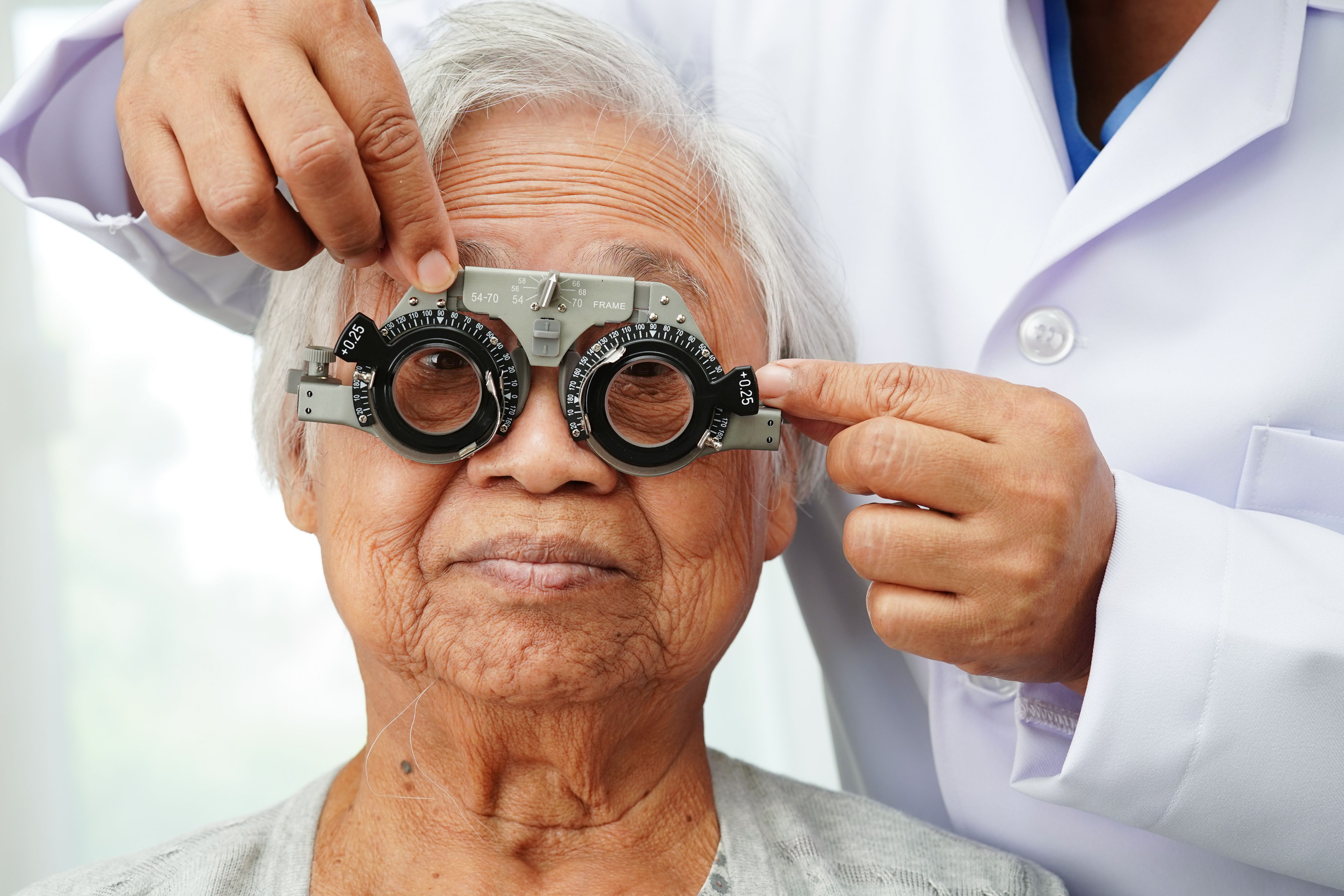 Optometrist checking Asian elderly woman ophthalmic vision eye test and using optical trial frame.