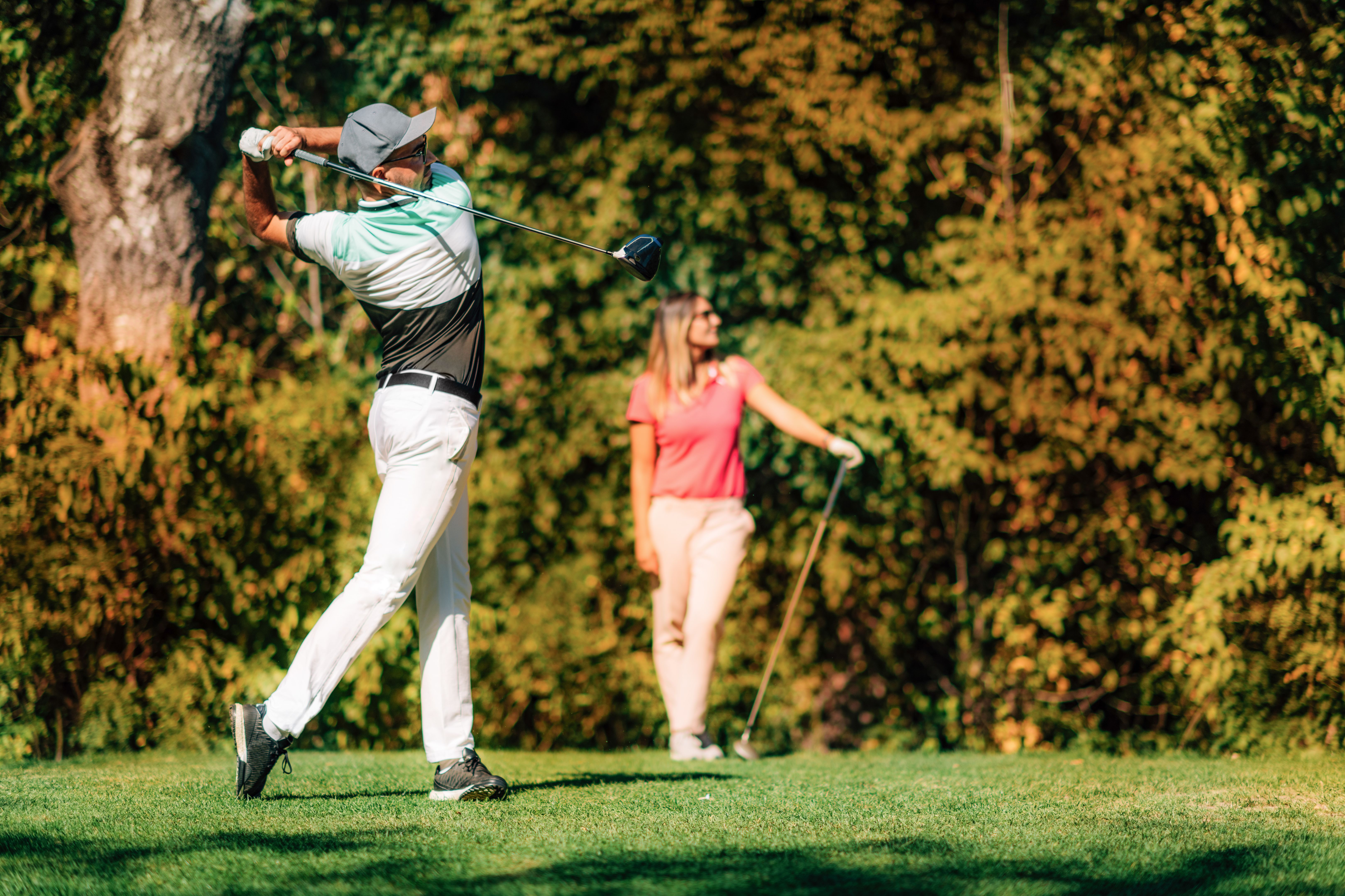 Golfing couple. Man in the swing position, lady following the ball in flight Golfing couple. Man in the swing position, lady following the ball in flight