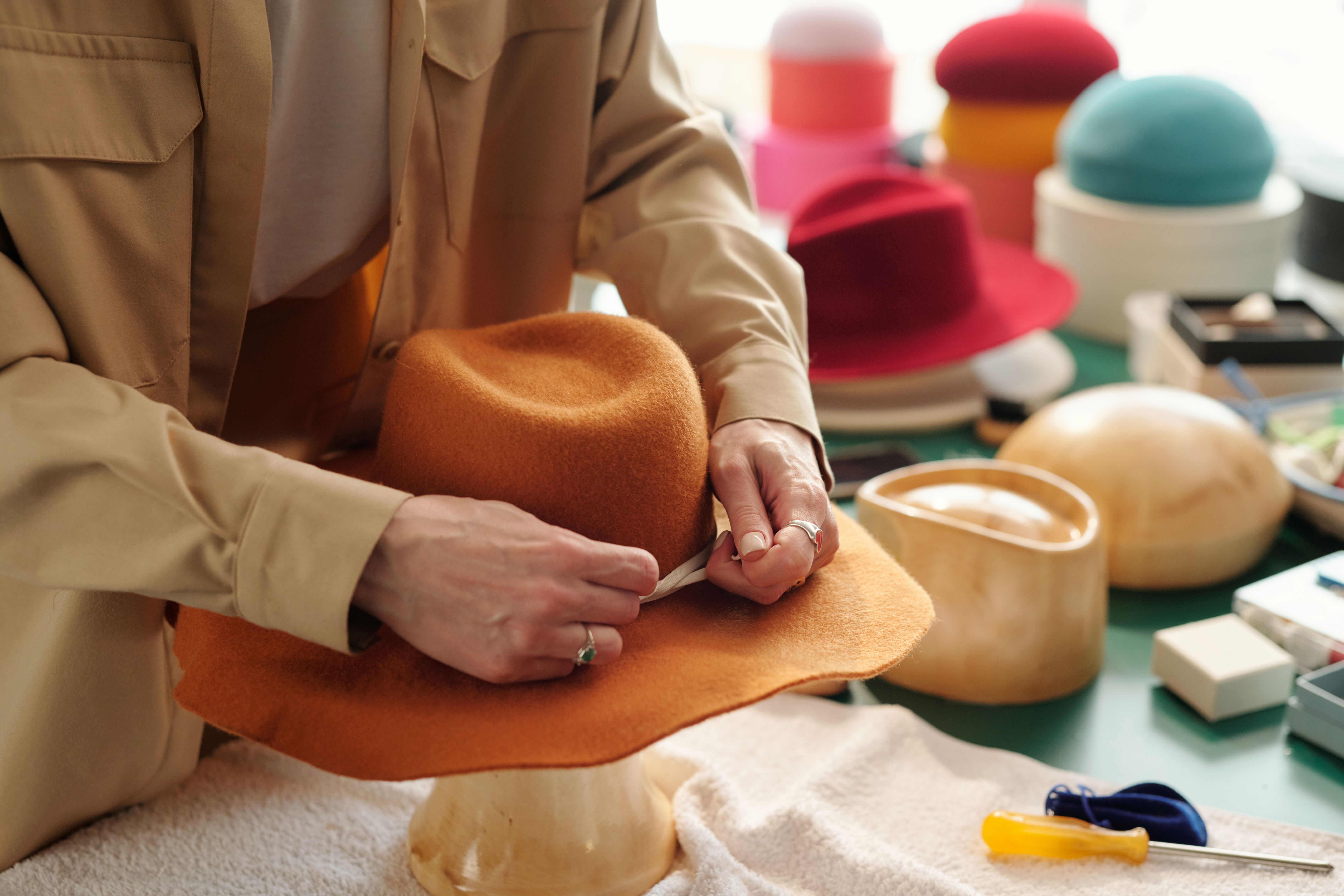 Close-up of young creative craftswoman fixing decorative shoelace arount hat