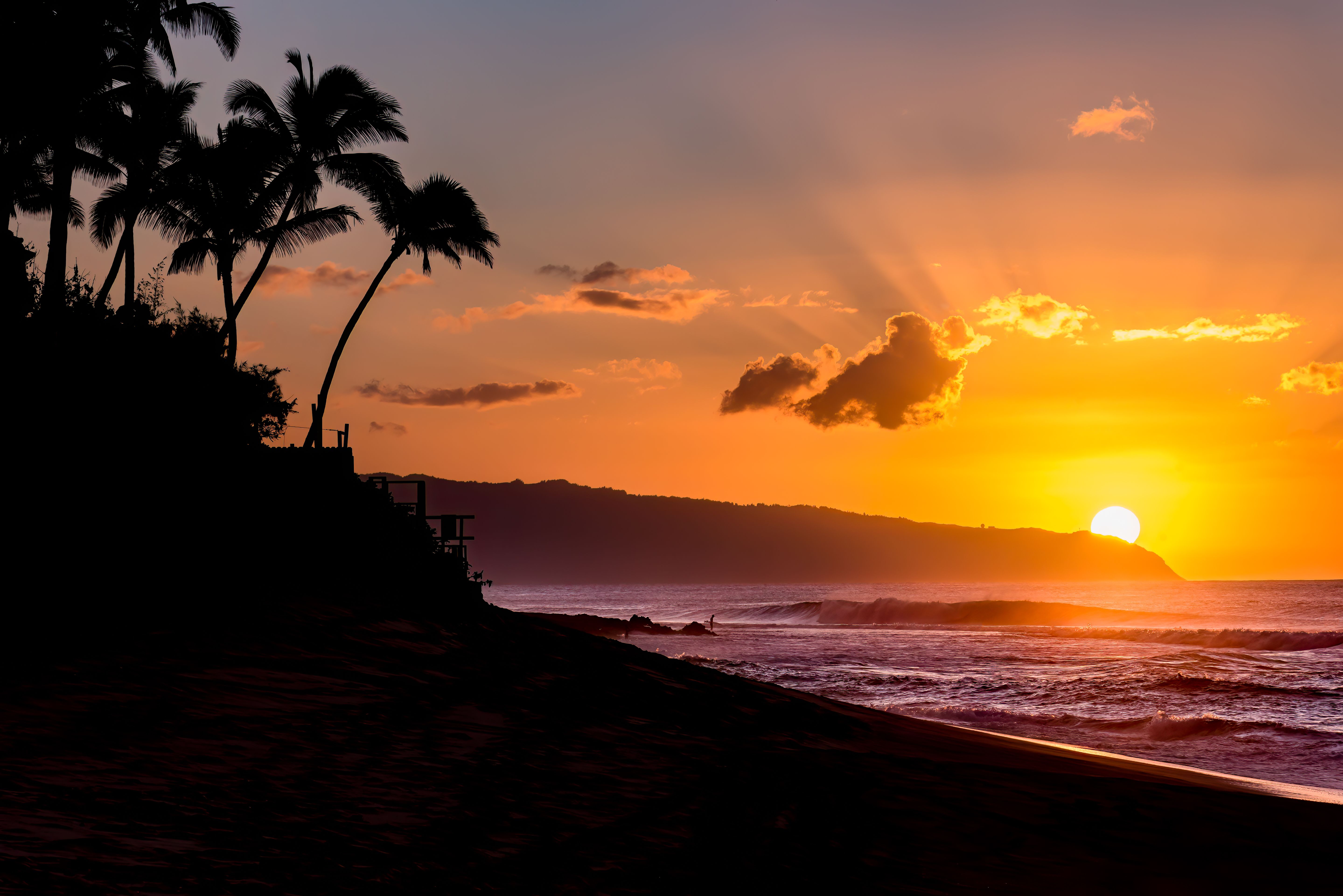 Sun setting over waves and palm trees on Sunset Beach, Hawaii