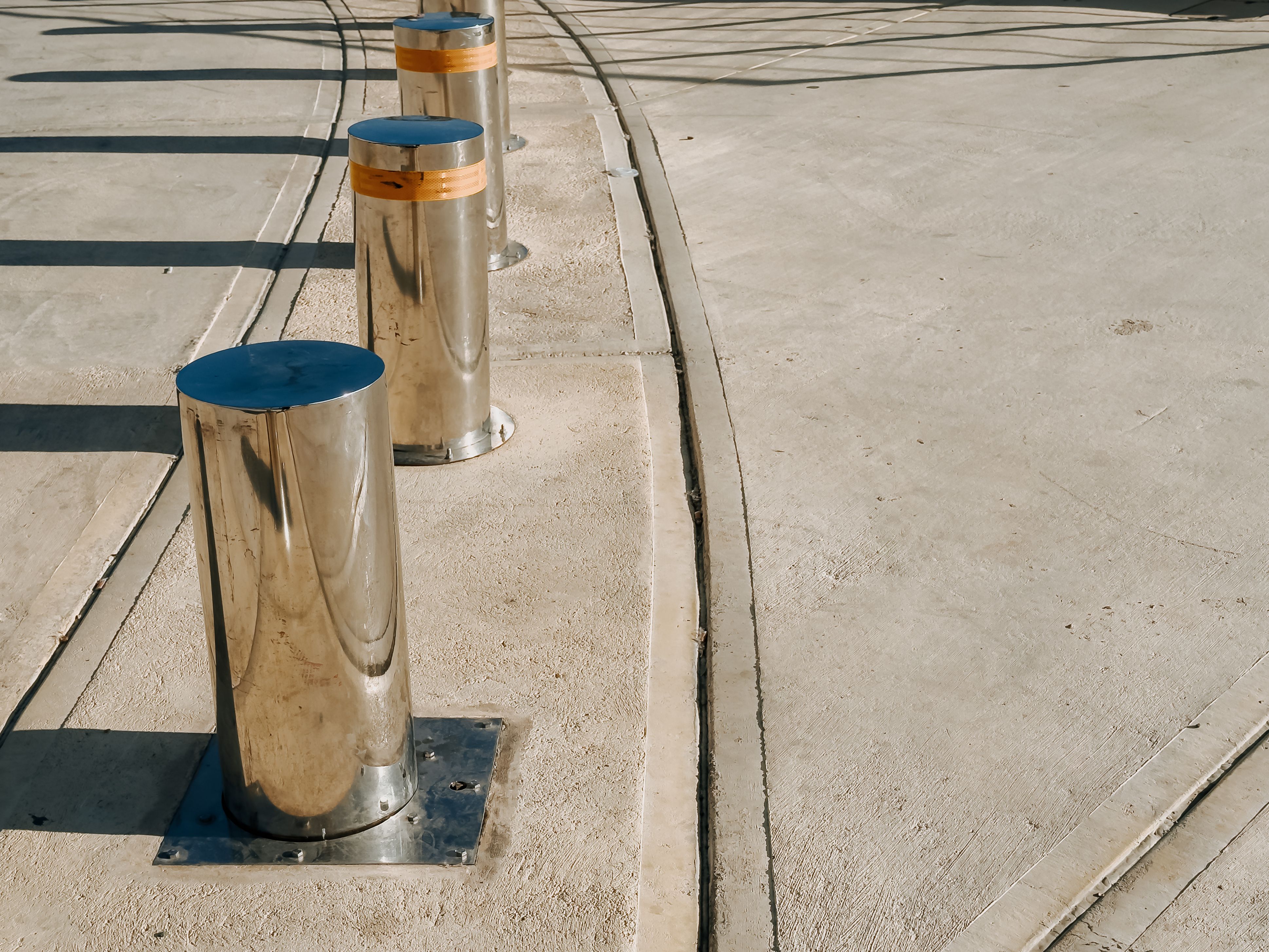 Urban security bollards on a sunny day casting long shadows on modern pavement