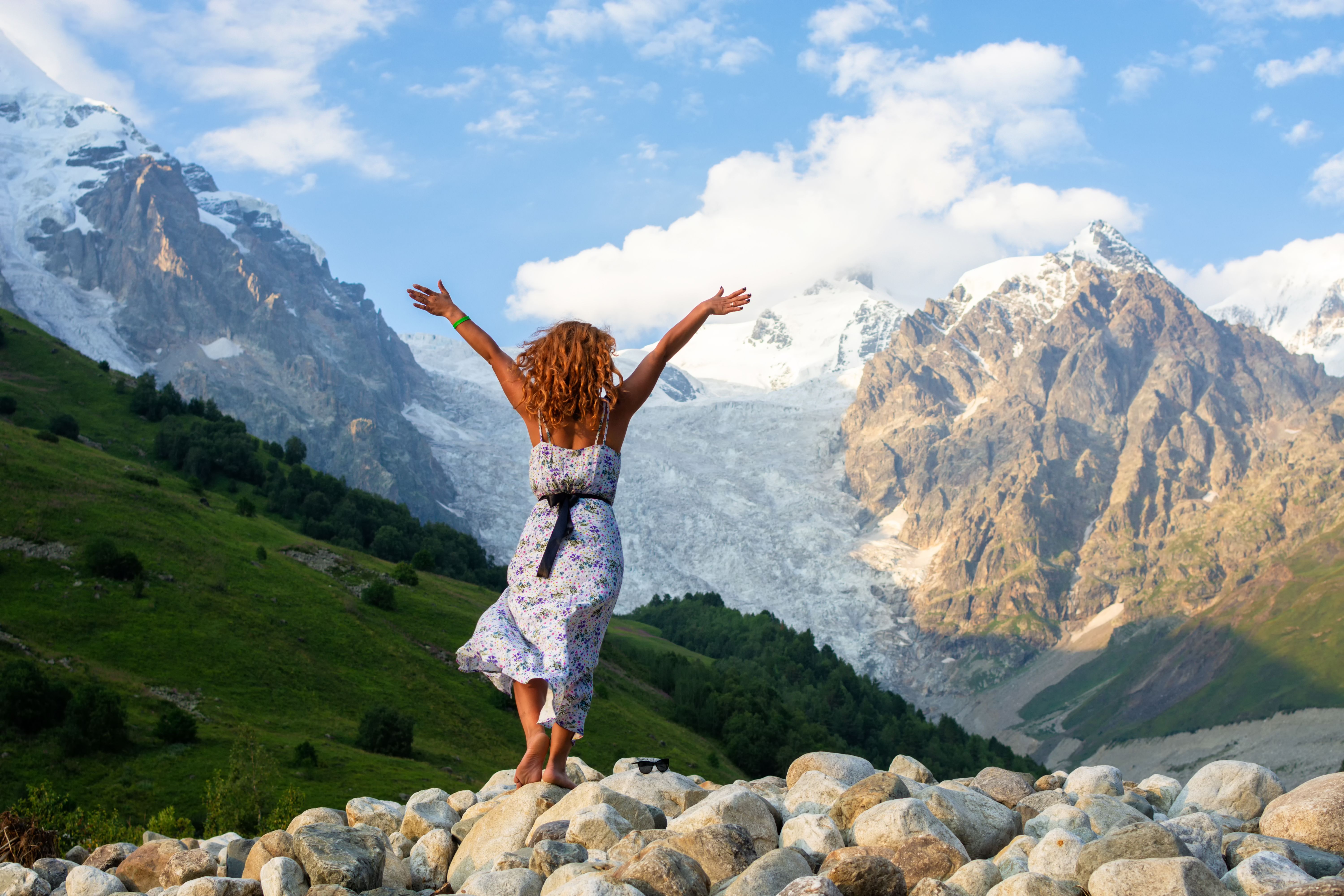 Young beautiful girl in a dress with red hair on the background of the Adishi glacier. Adish Glacier in Svaneti and the Caucasus Mountains.