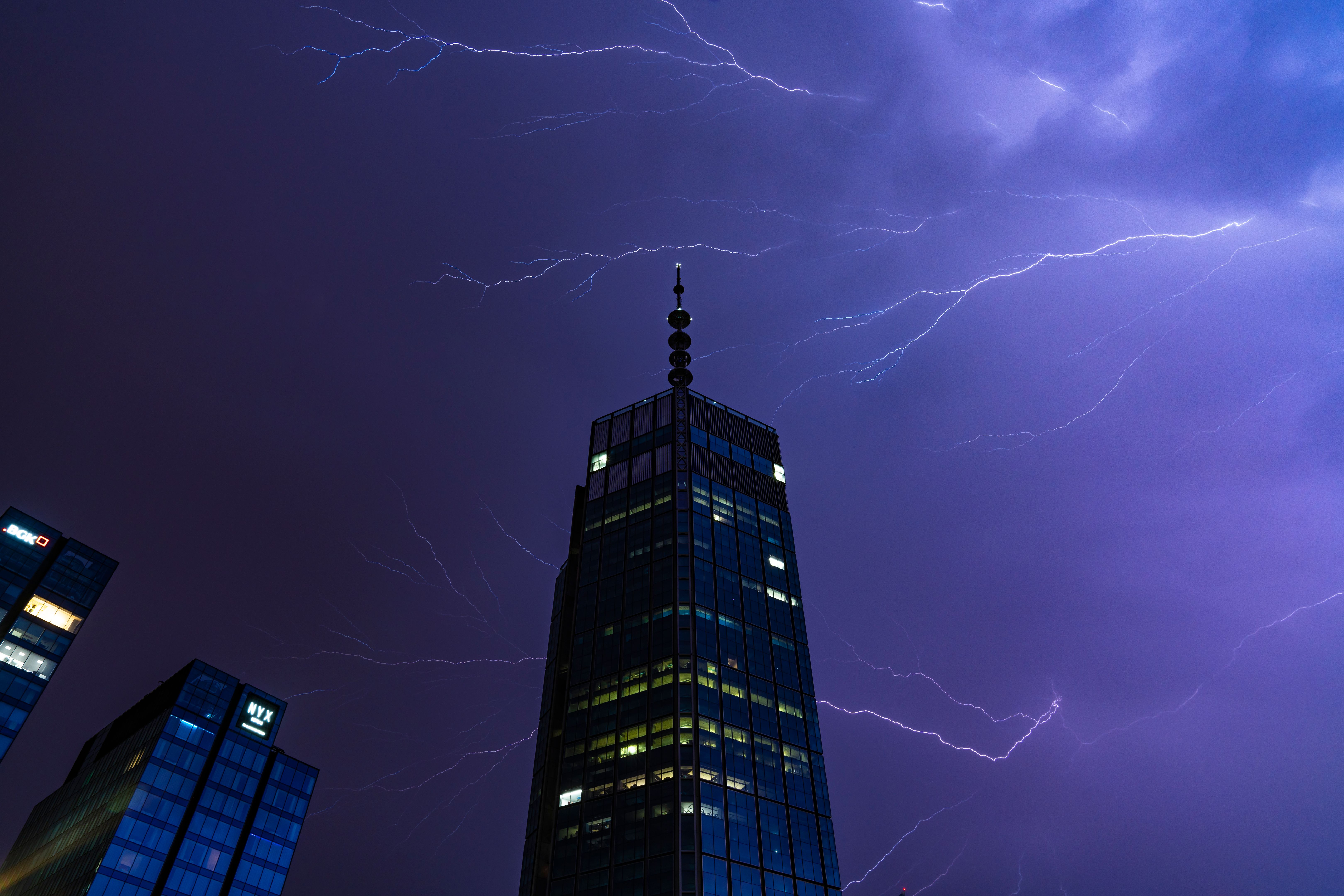 Lightning at night above a tall glass skyscraper. The tallest skyscraper in Europe is located in the city of Warsaw, Poland.
