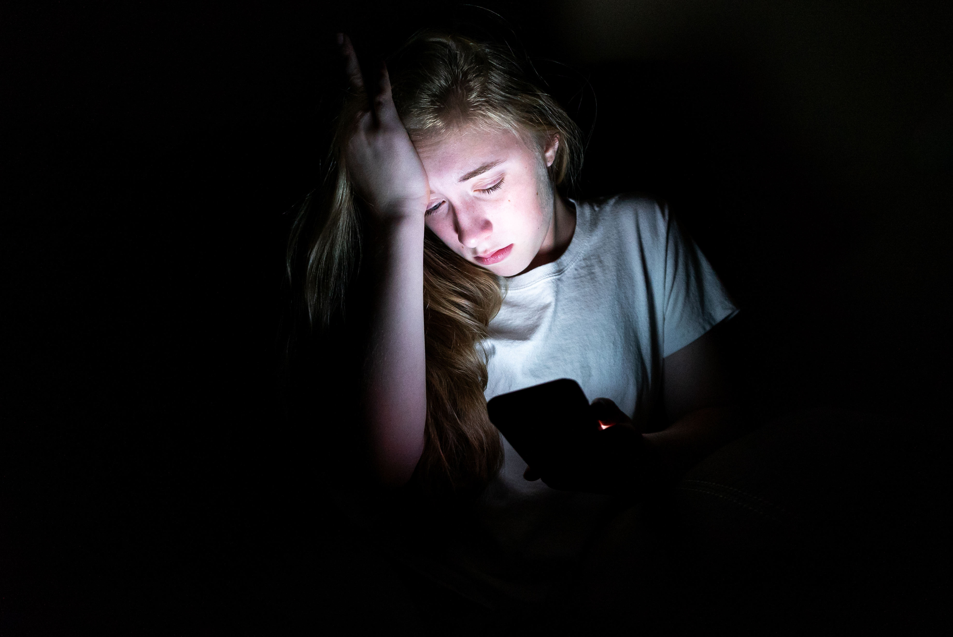Upset girl on her smartphone in the dark.