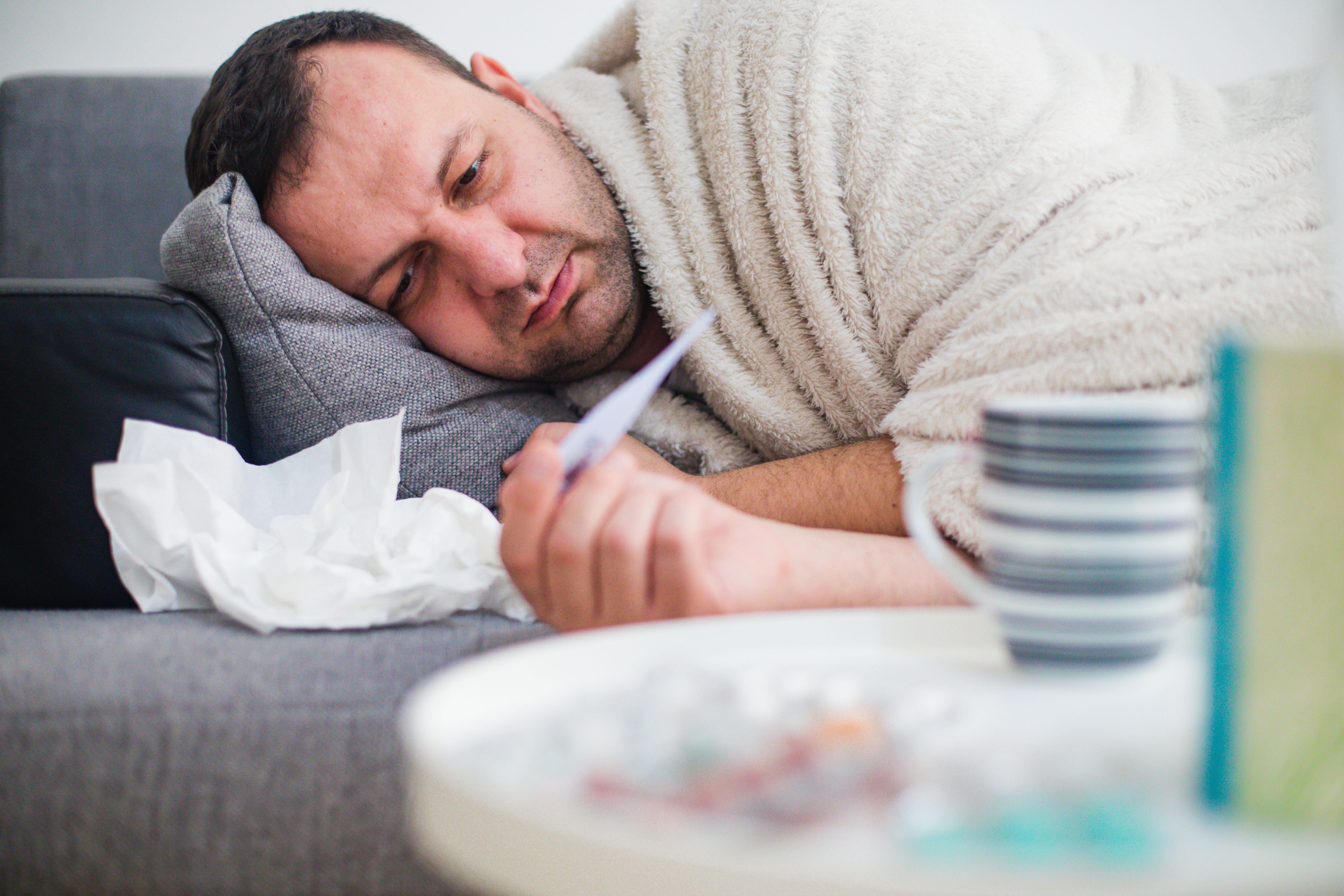 Hombre enfermo en la fiebre de chequeo de la cama con termómetro Hombre enfermo en la fiebre de chequeo de la cama con termómetro