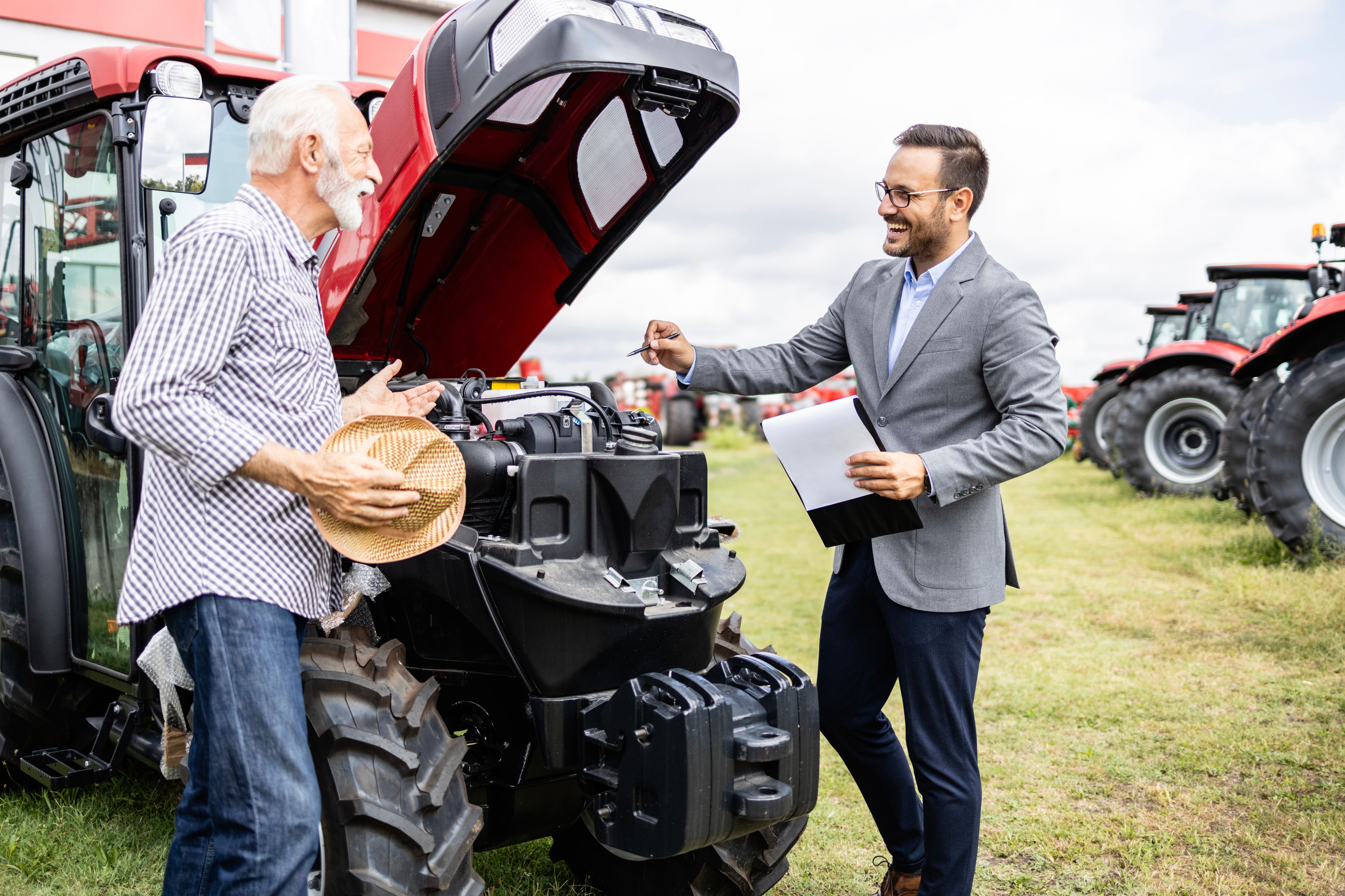Salesman presenting engine specification and power of the tractor machine to the buyer. Investing in agriculture. Salesman presenting engine specification and power of the tractor machine to the buyer. Investing in agriculture.