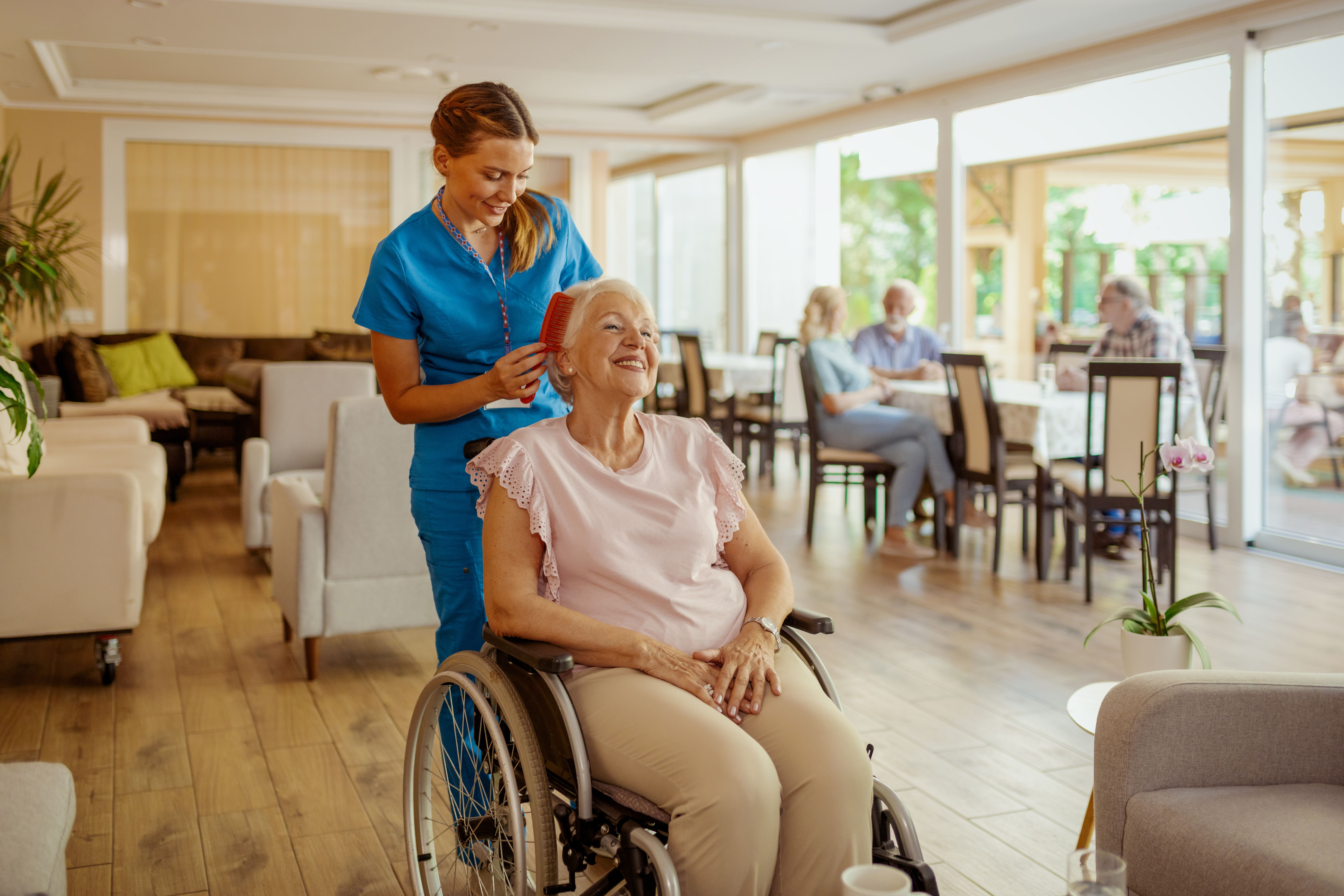 Female smiling caregiver helps a senior woman fix her hair in an assisted living facility.