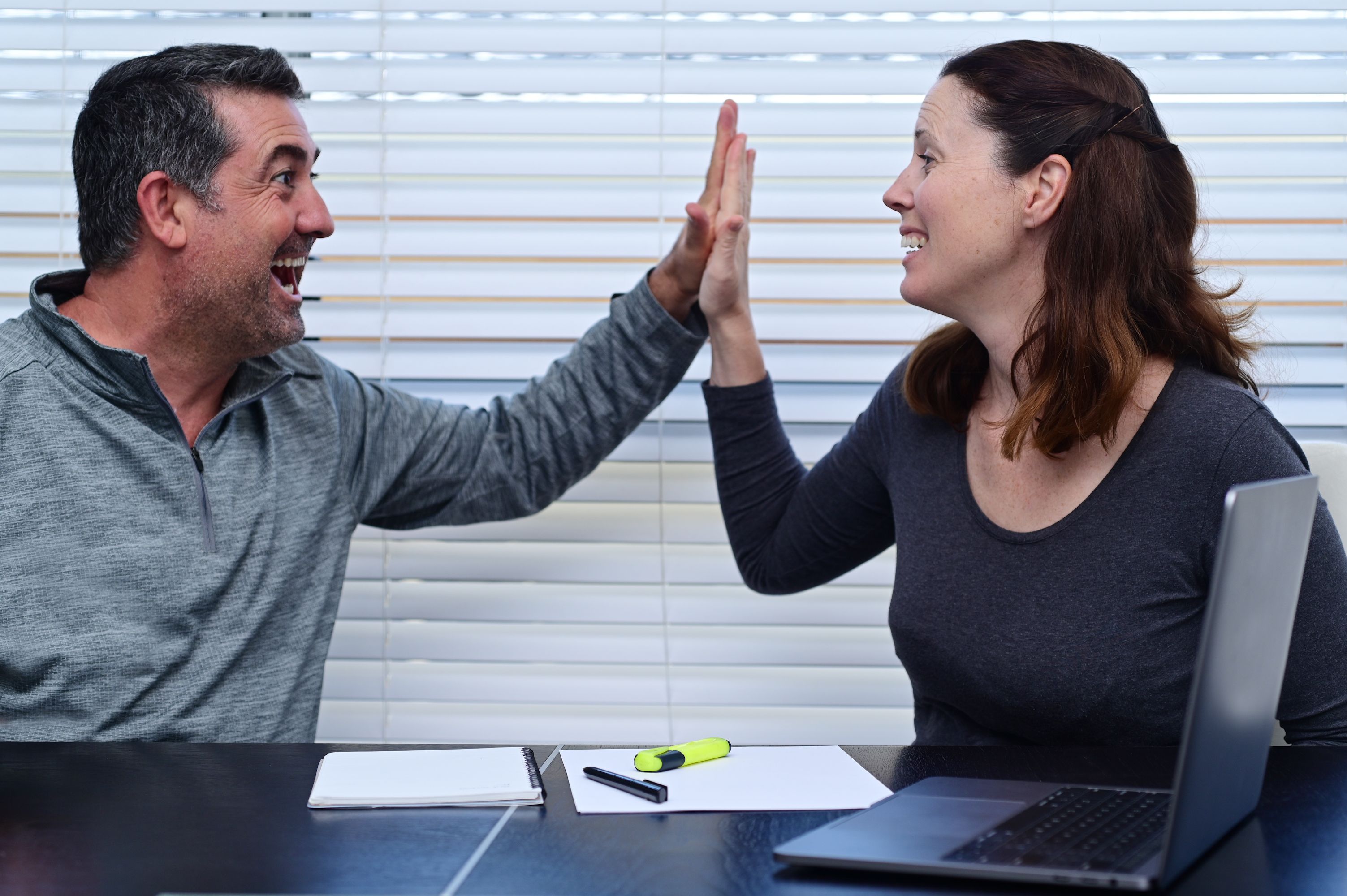Happy couple high five after looking at positive financial data on laptop