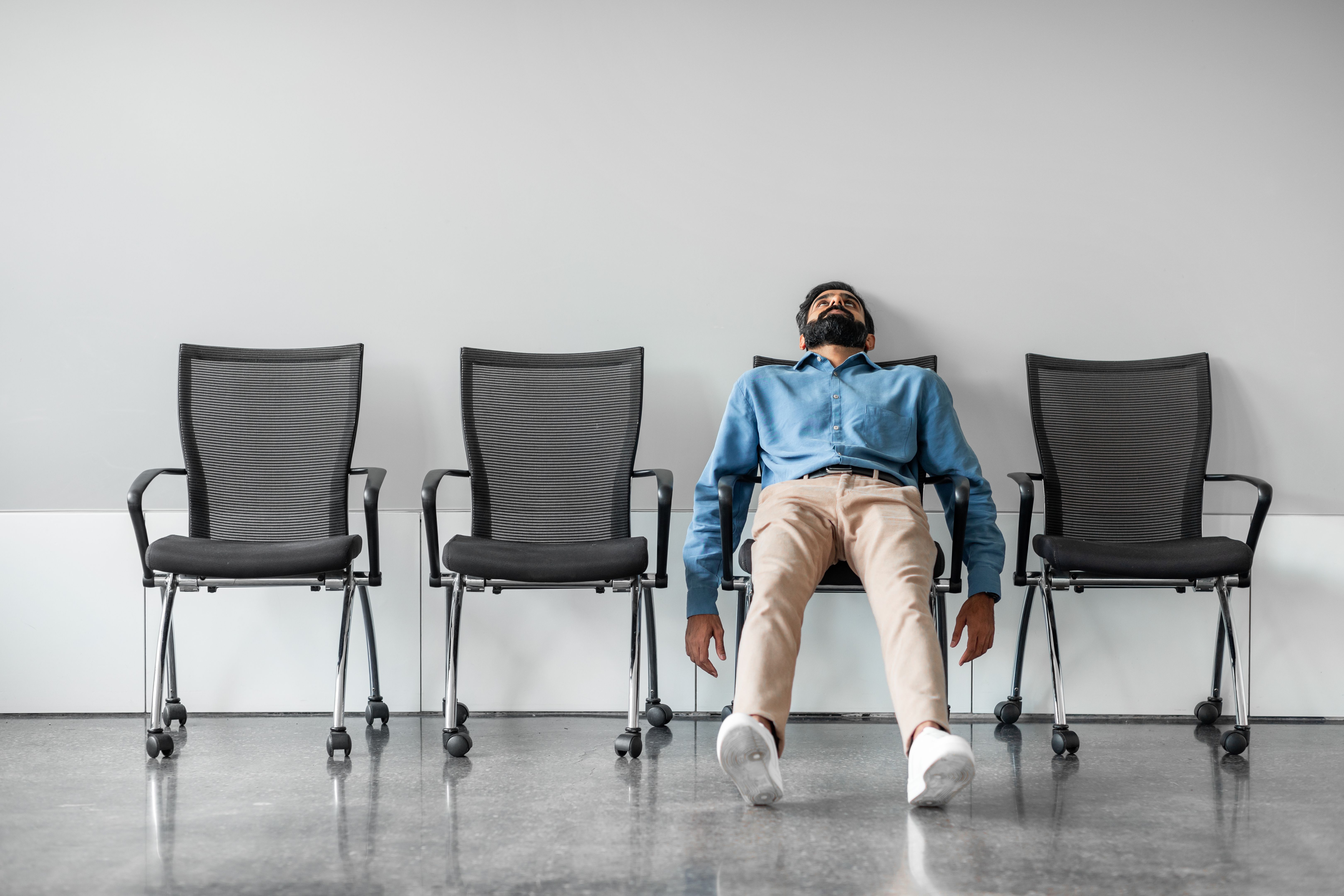Bored and disappointed male indian employee sitting in waiting room on row of chairs, full length shot Bored and disappointed male indian employee sitting in waiting room on row of chairs, full length shot