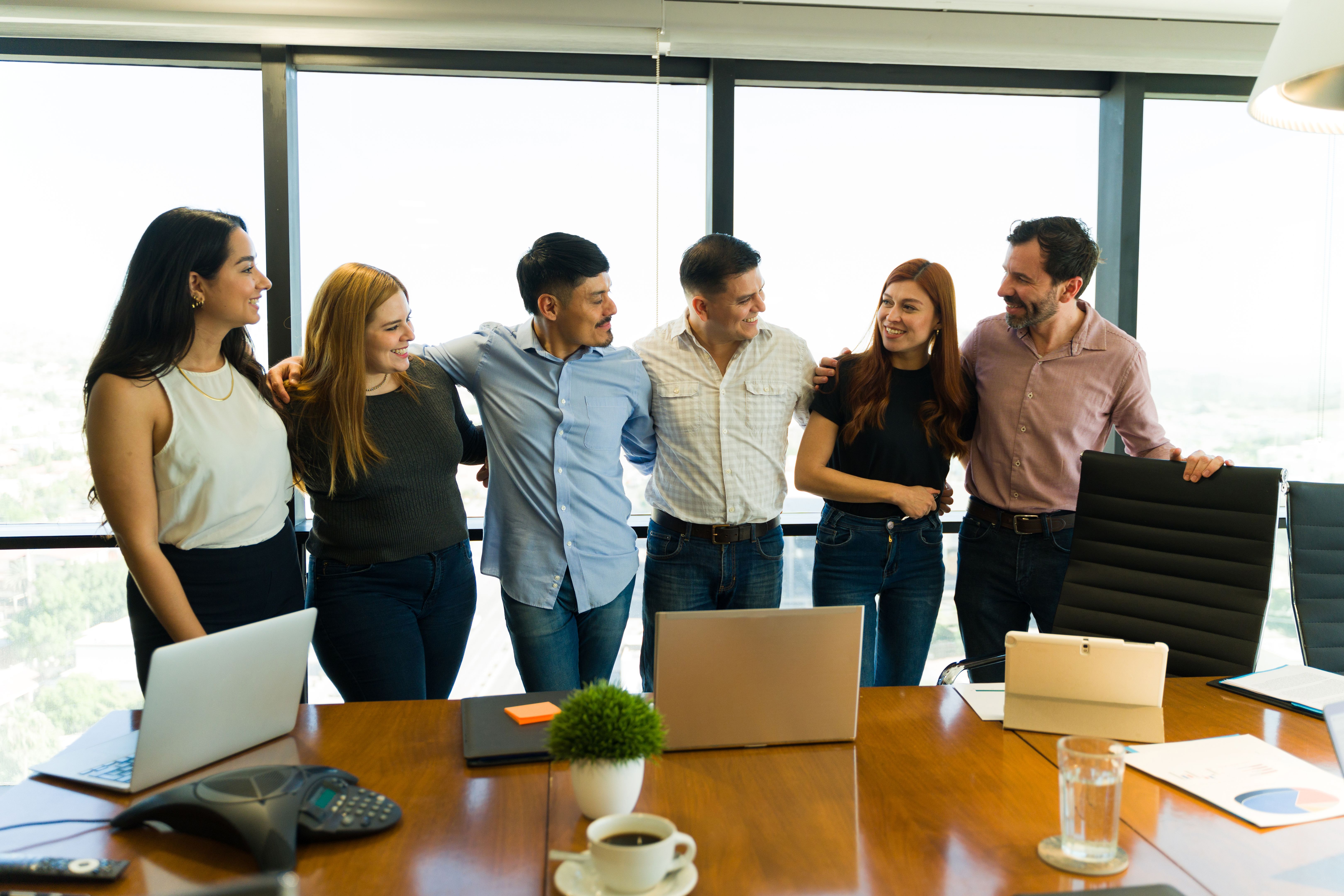 Group of businesspeople in casual clothes embracing each other and looking happy Group of businesspeople in casual clothes embracing each other and looking happy