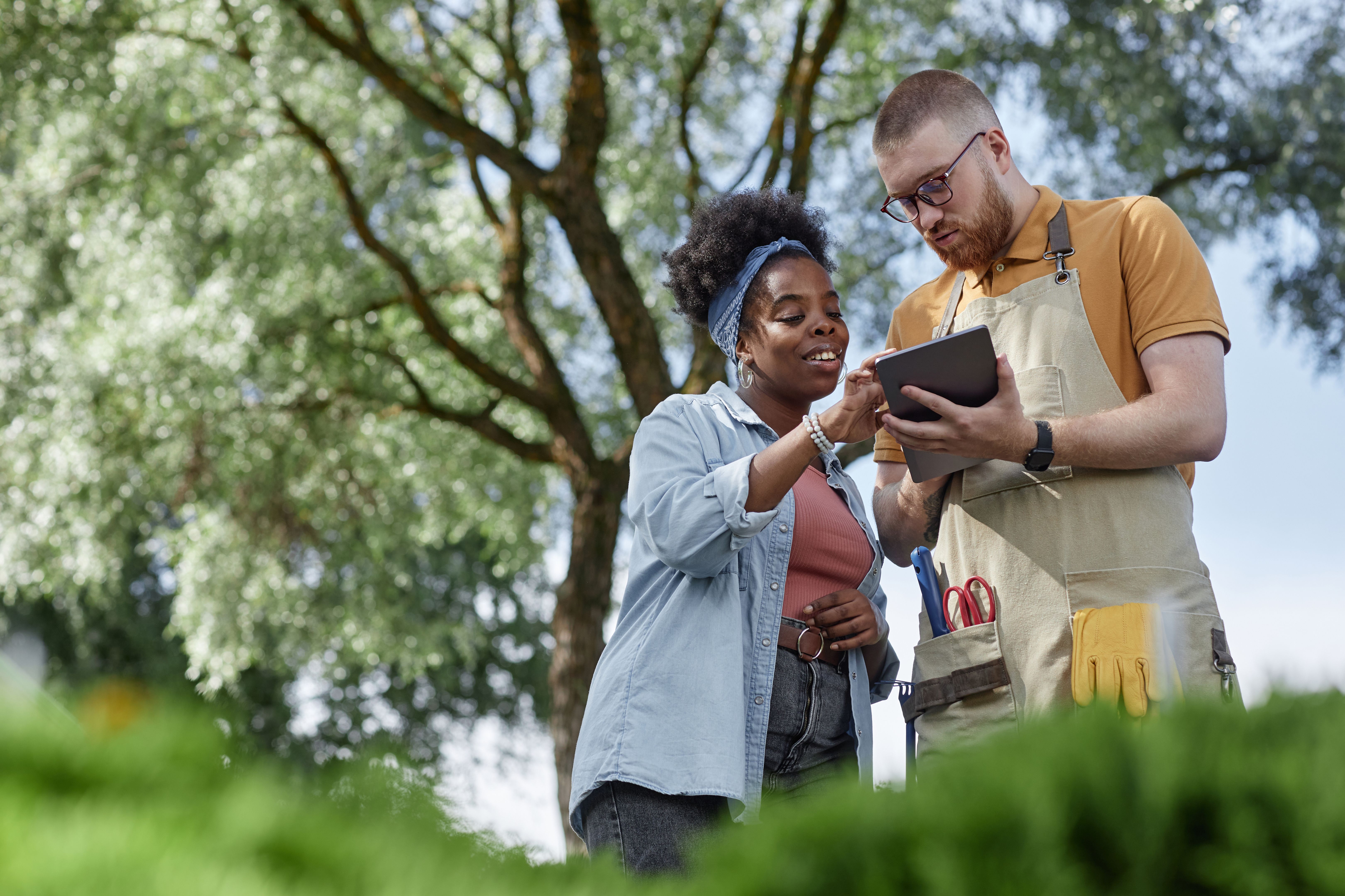 Smiling Female Black Landscape Architect Using Tablet Talking to Worker in Garden Center