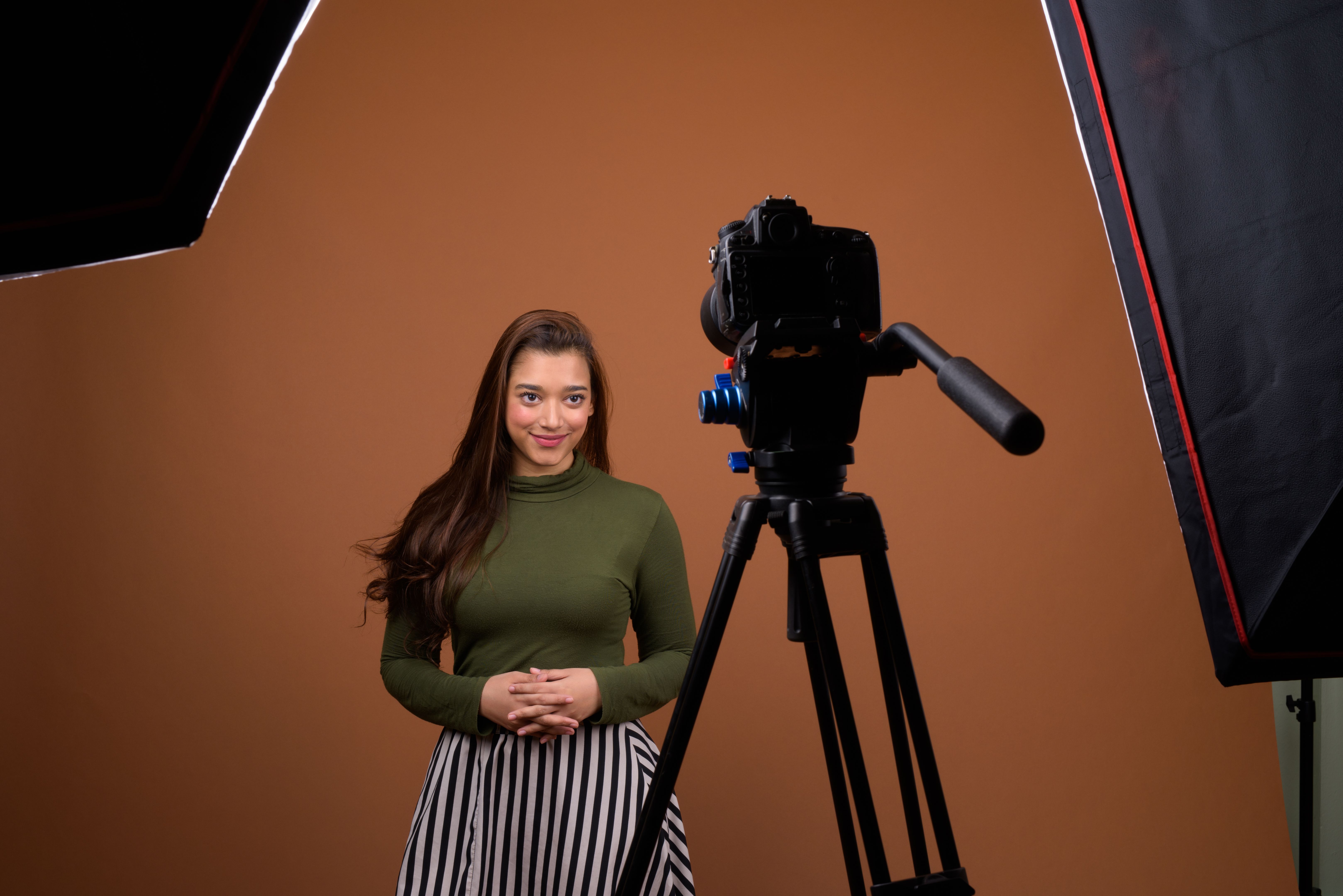 Studio shot of young beautiful Indian woman vlogging against colored background