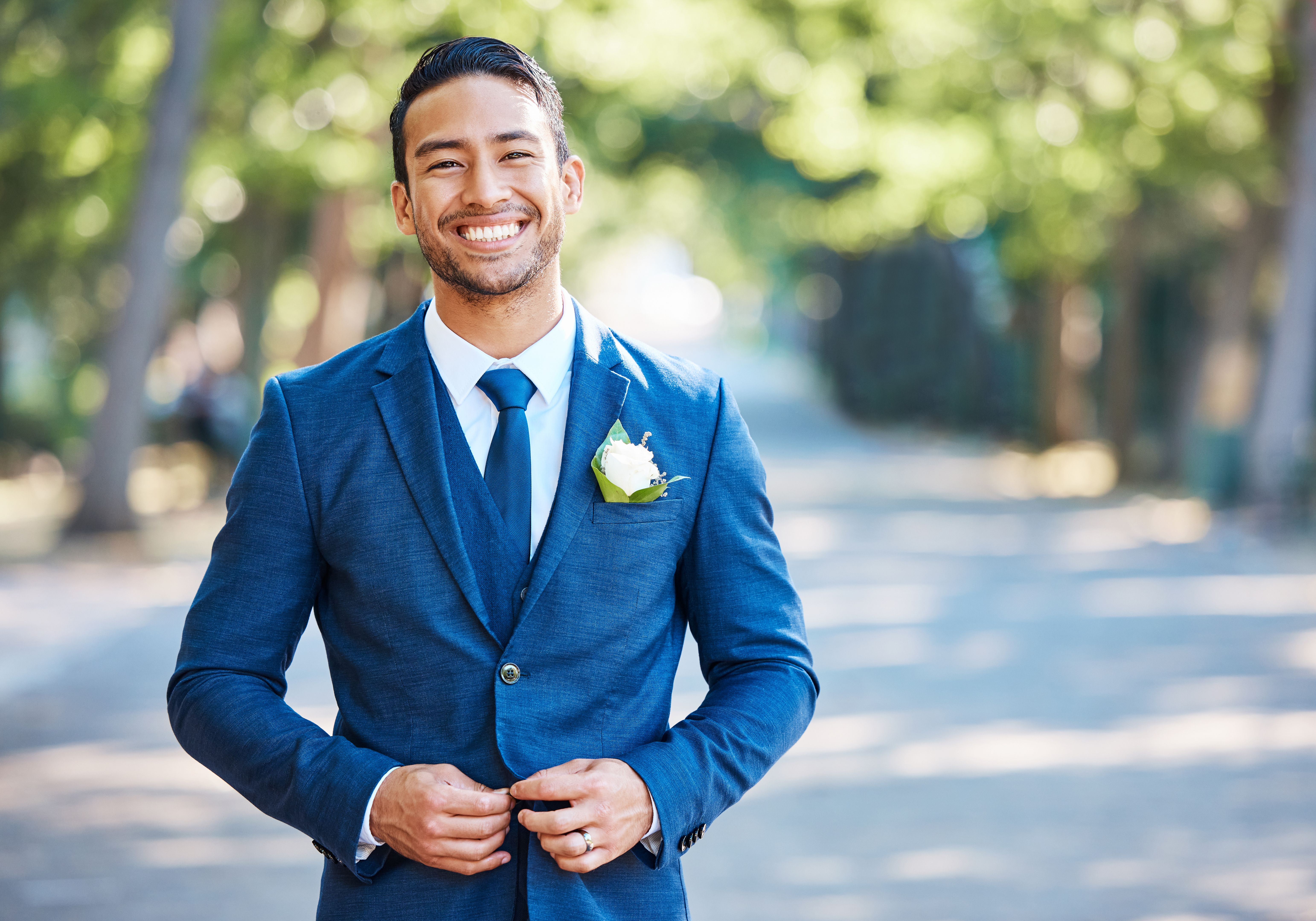 Handsome groom wearing a blue suit with a white shirt and tie. Bridegroom fastening his jacket while standing outdoors on a sunny day Handsome groom wearing a blue suit with a white shirt and tie. Bridegroom fastening his jacket while standing outdoors on a sunny day