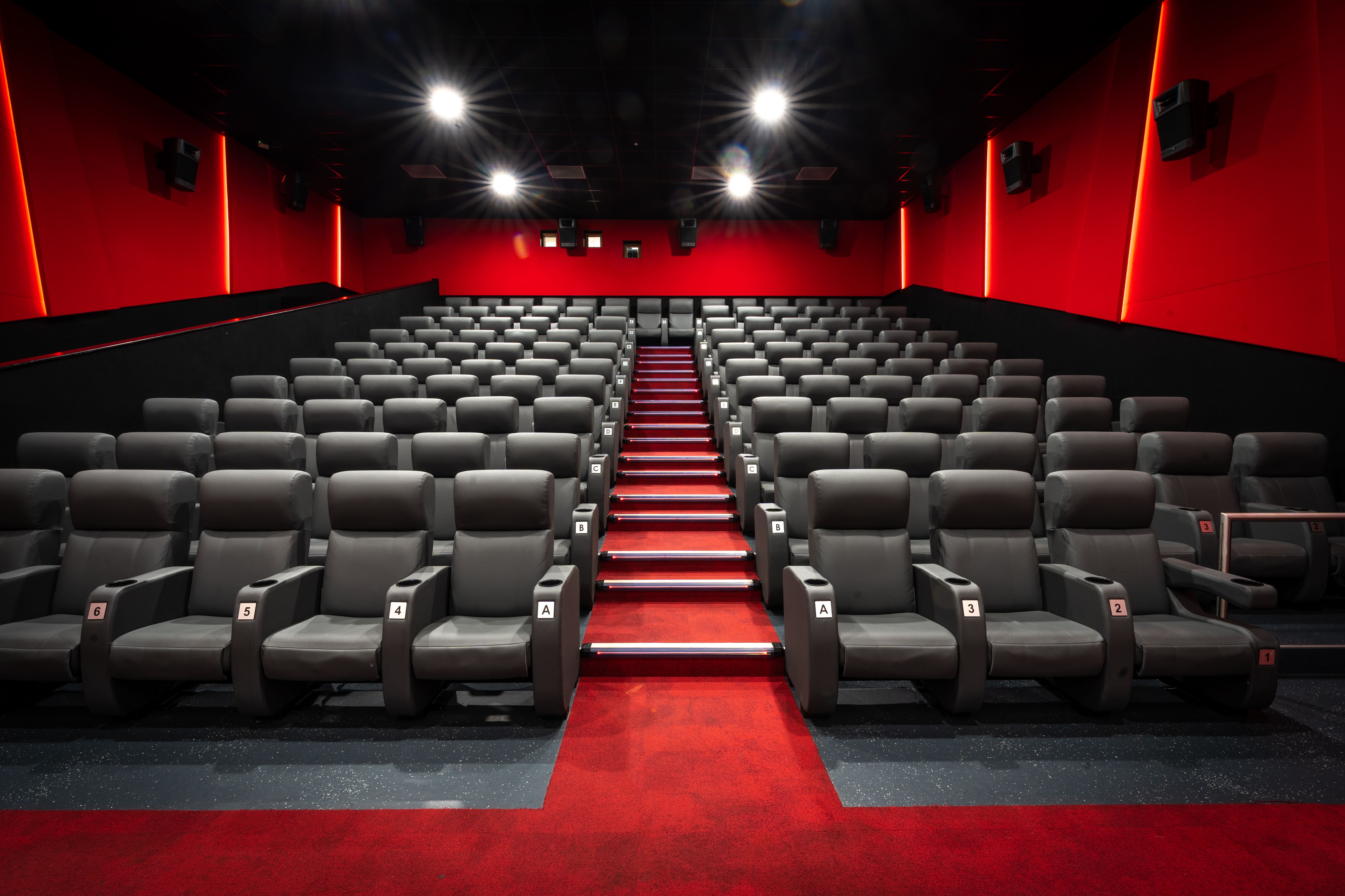 a modern empty cinema movie theatre with rows of dark seating and spot lights shining down with red walls a modern empty cinema movie theatre with rows of dark seating and spot lights shining down with red walls