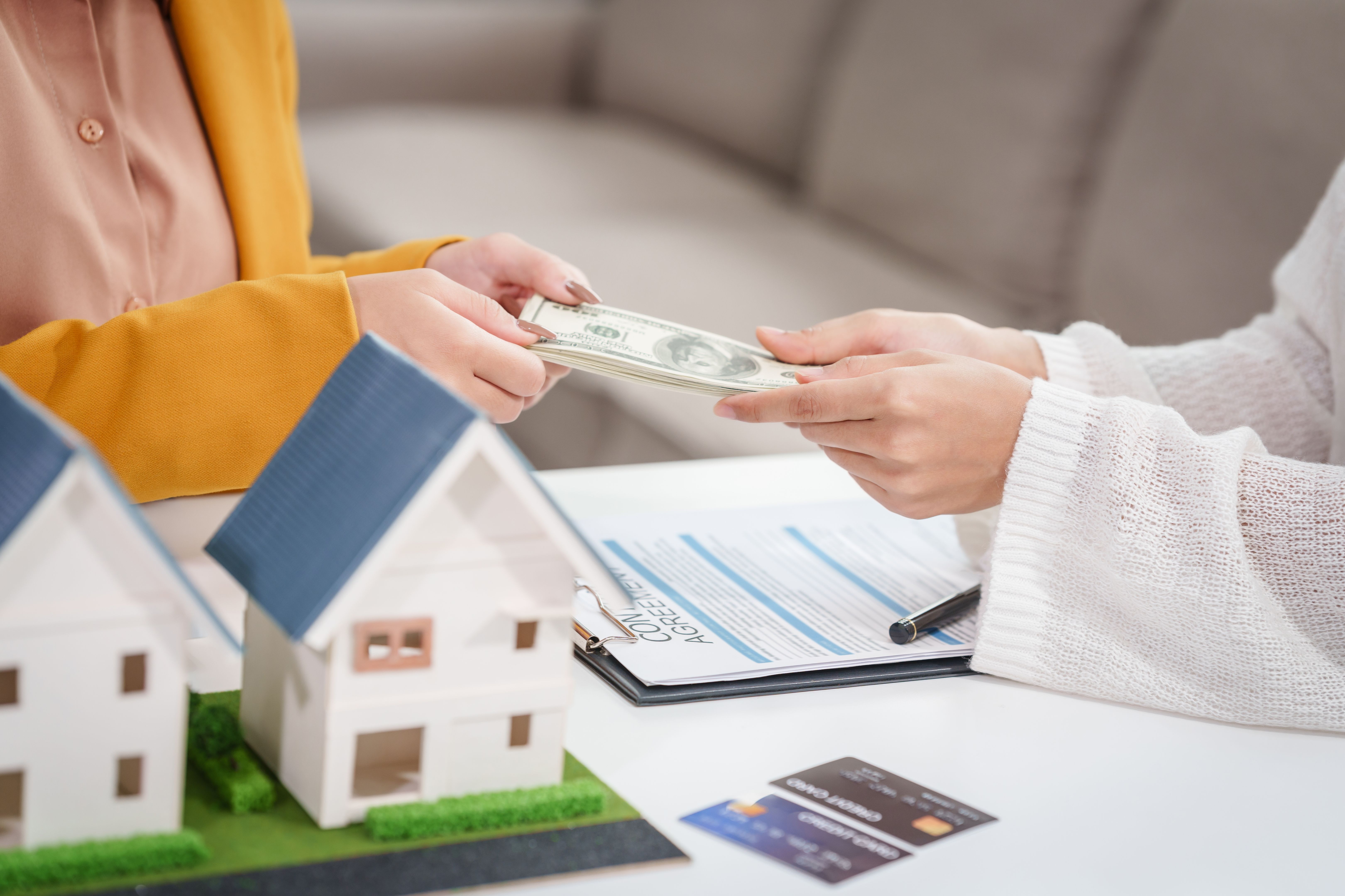 Asian businesswoman discusses home purchase contracts with clients at her desk, focusing on loans, mortgages, and other financial aspects of real estate transactions.