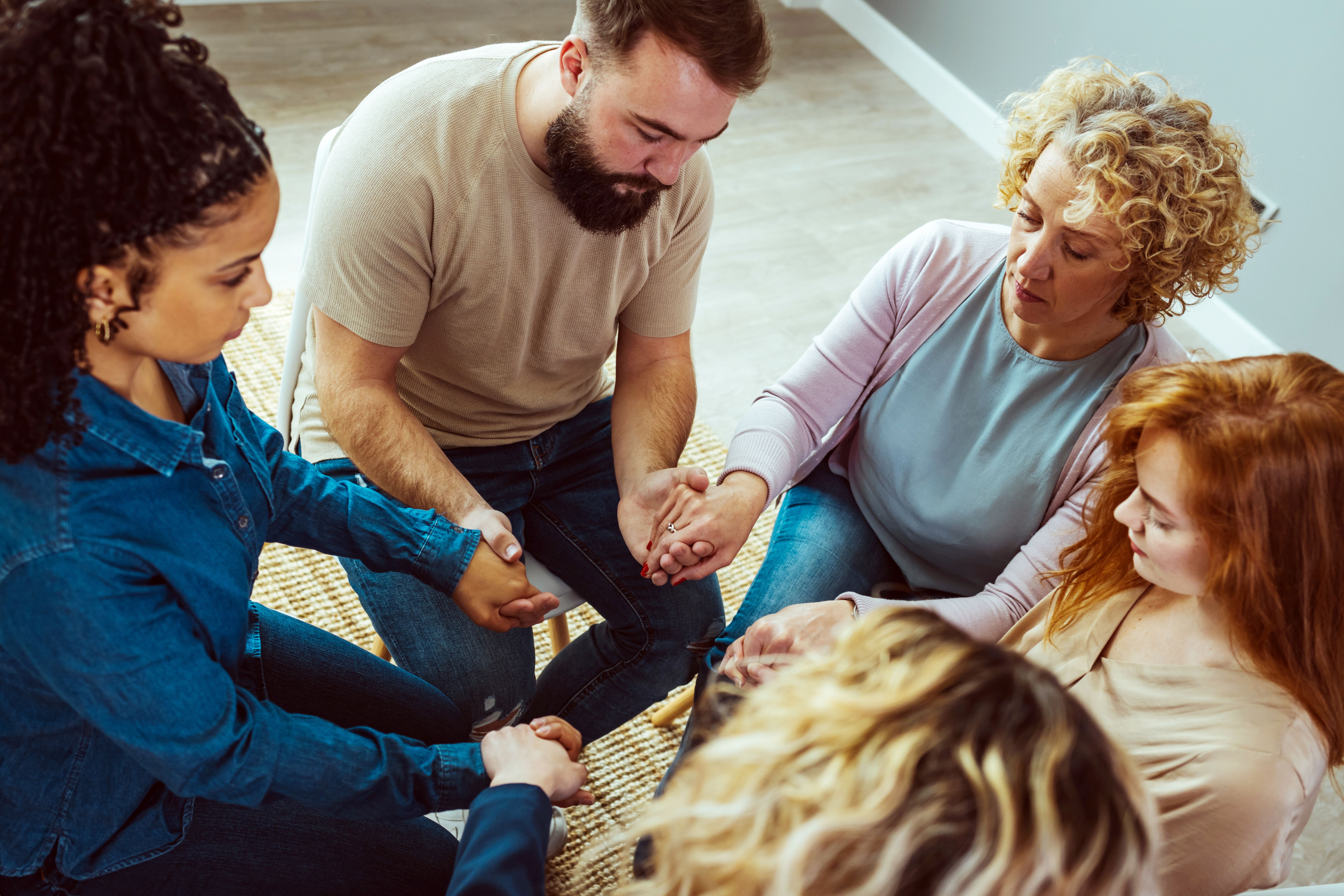 Close-up of a group of diverse people sitting in a circle and holding hands together during a support group meeting