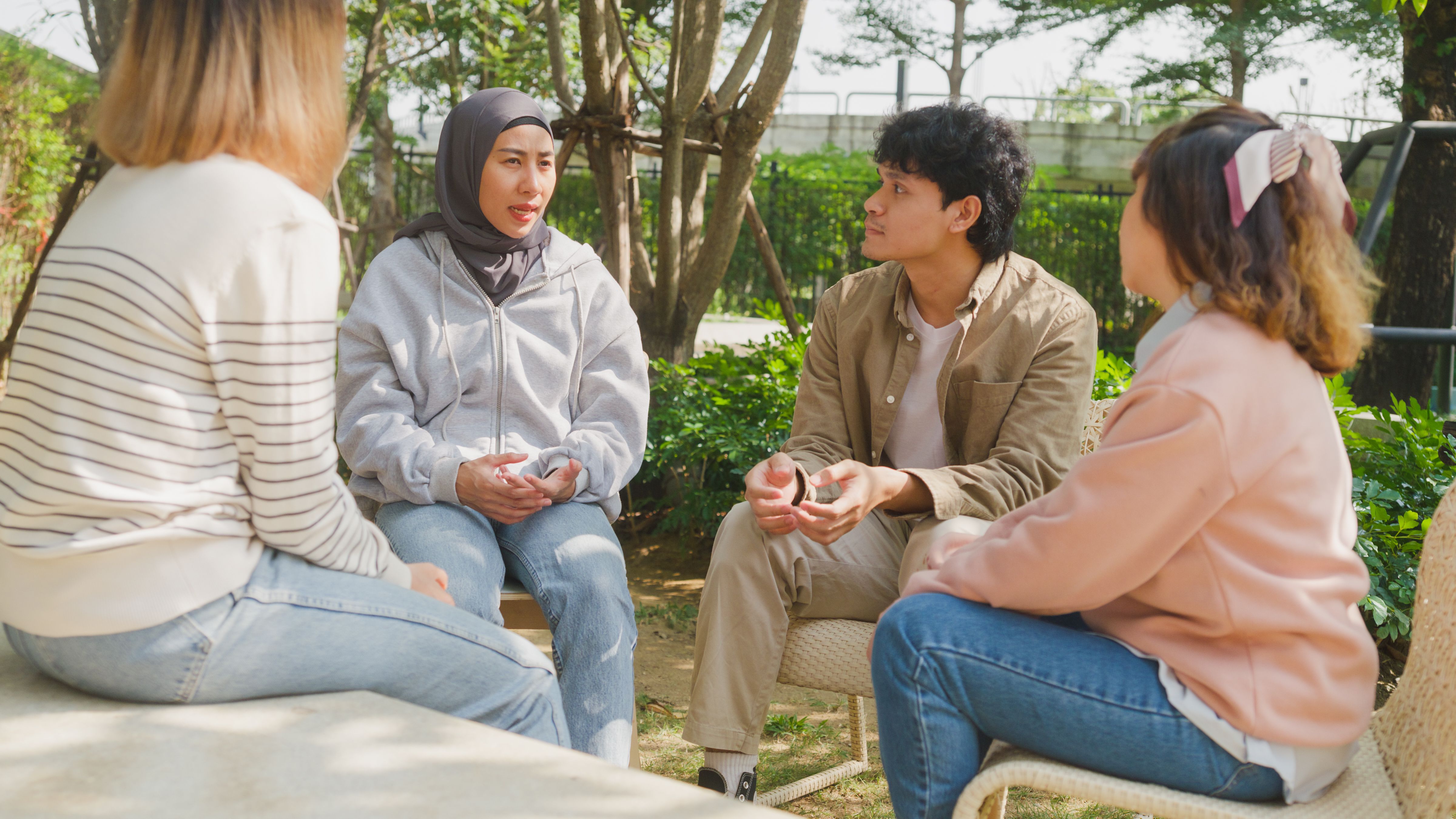 Small Asian group of people sit in a close circle and talk to a therapist in park. Smile people sharing story happy speak diverse people sitting in circle at group therapy session psychologist.