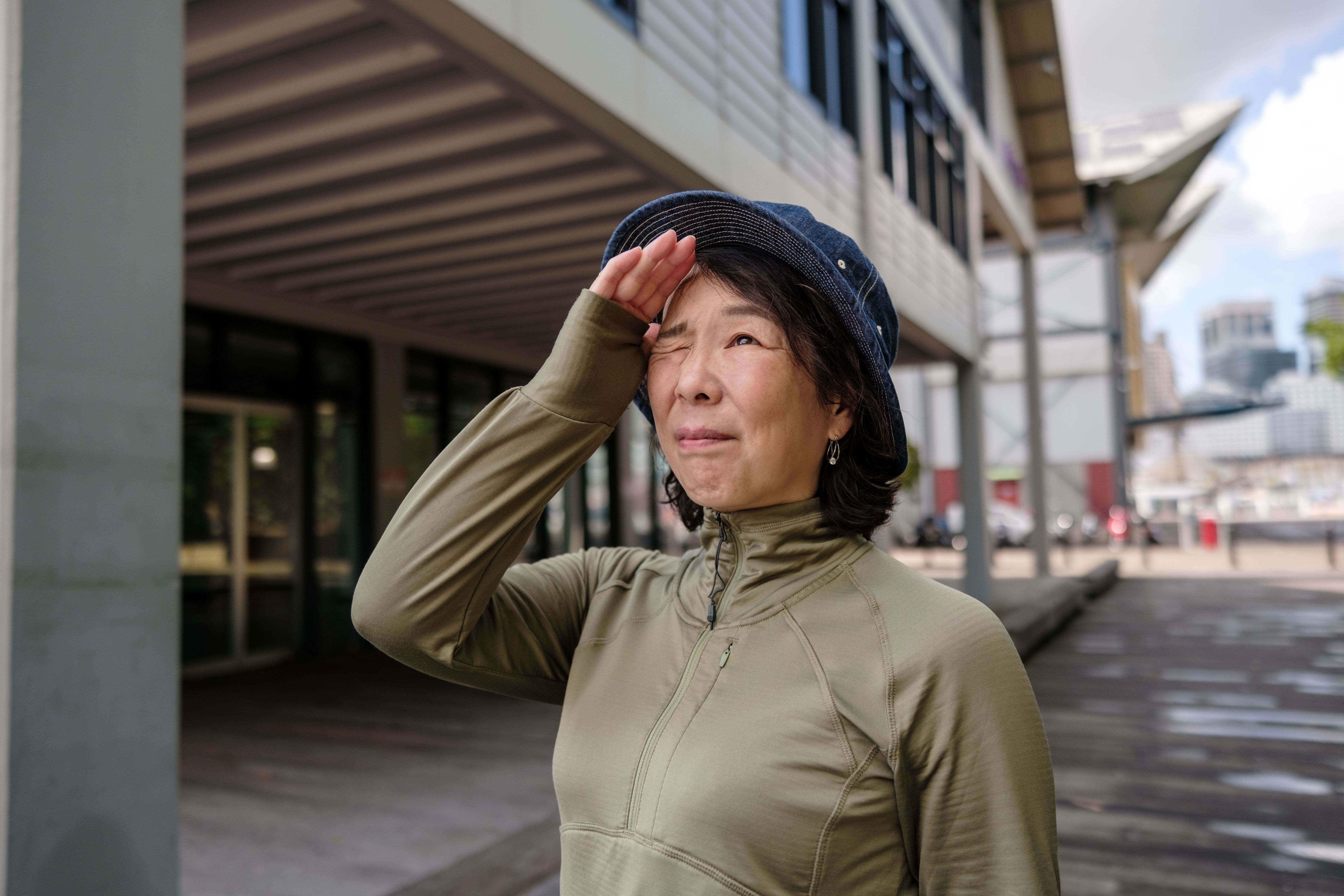 Asian woman shading her eyes and looking up into the sky