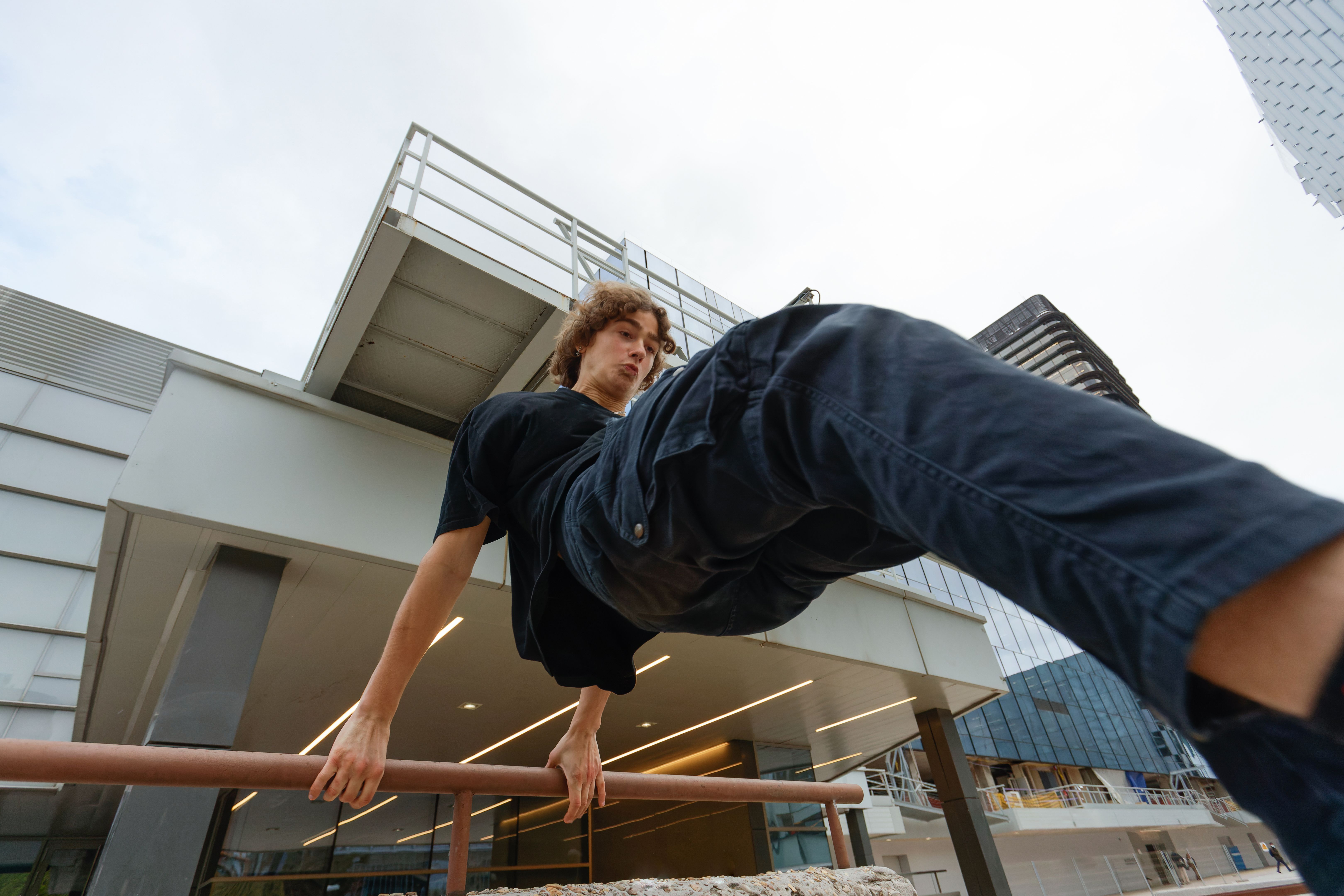 View from below of a young man jumping over a railing in the city