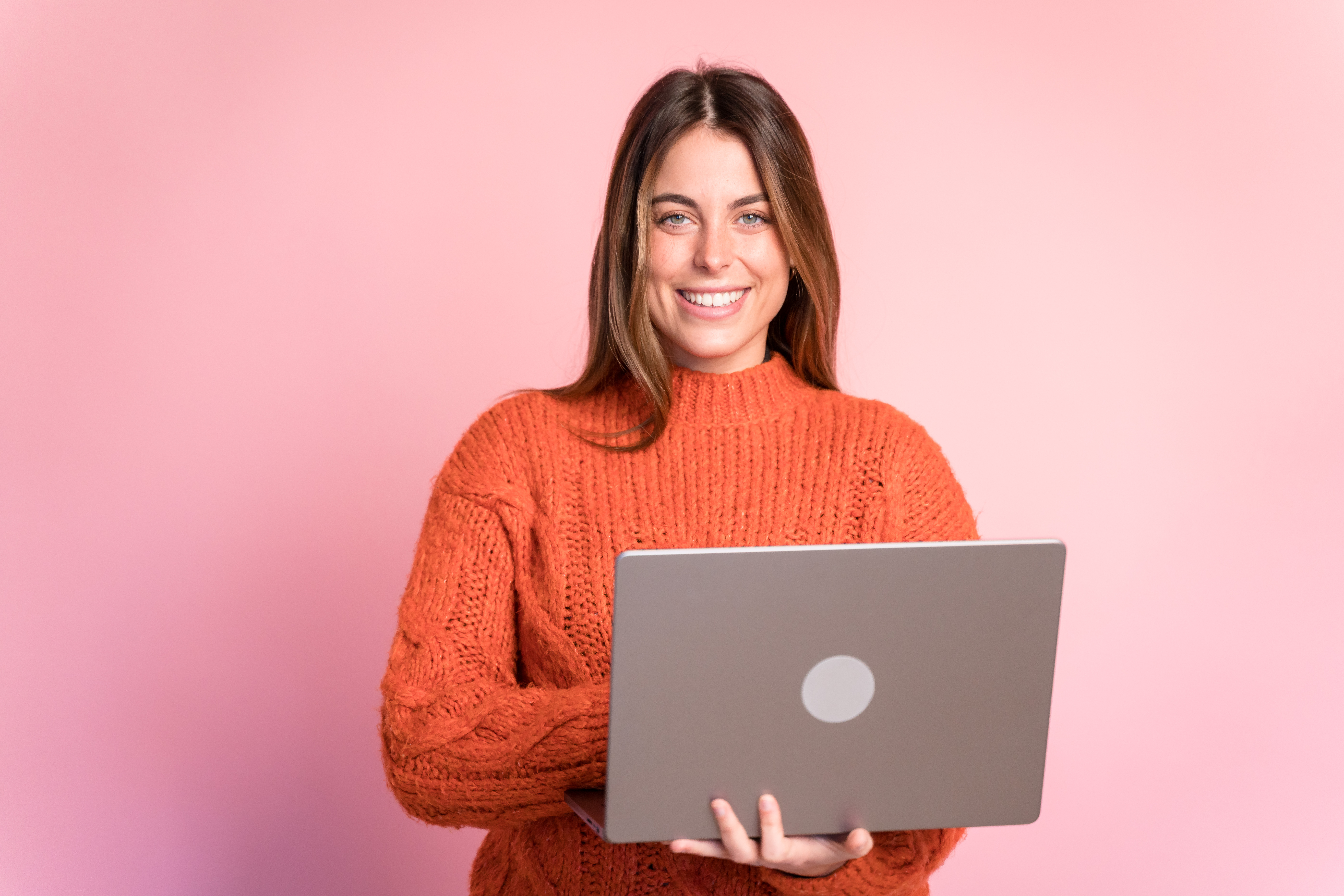 Smiling woman with laptop against pink background