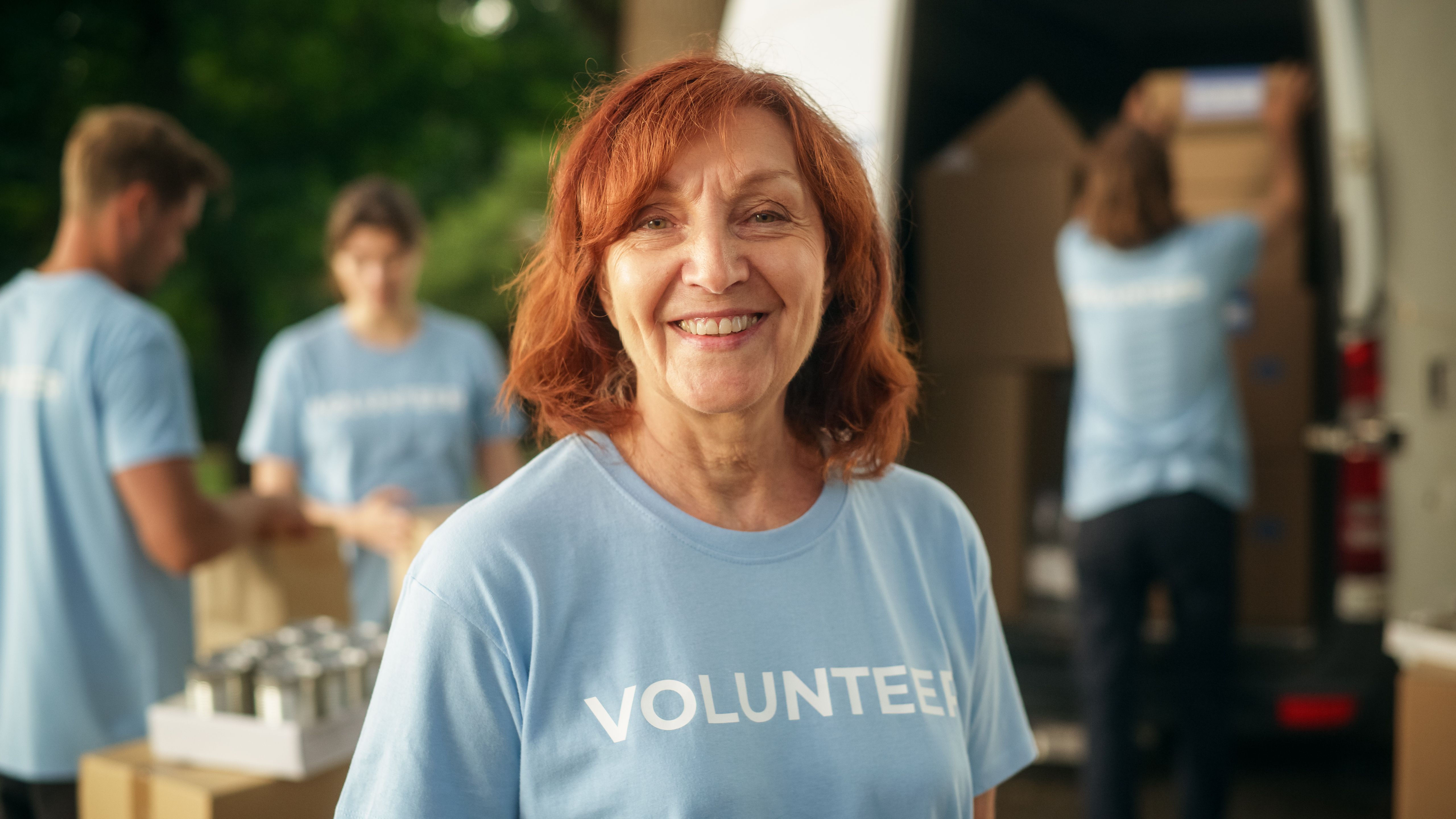 Portrait of a Happy Helpful Middle Aged Female Volunteer. Adult Caucasian Woman in Blue T-Shirt, Smiling, Looking at Camera. Humanitarian Aid, Donations Center and Volunteering Concept. Portrait of a Happy Helpful Middle Aged Female Volunteer. Adult Caucasian Woman in Blue T-Shirt, Smiling, Looking at Camera. Humanitarian Aid, Donations Center and Volunteering Concept.