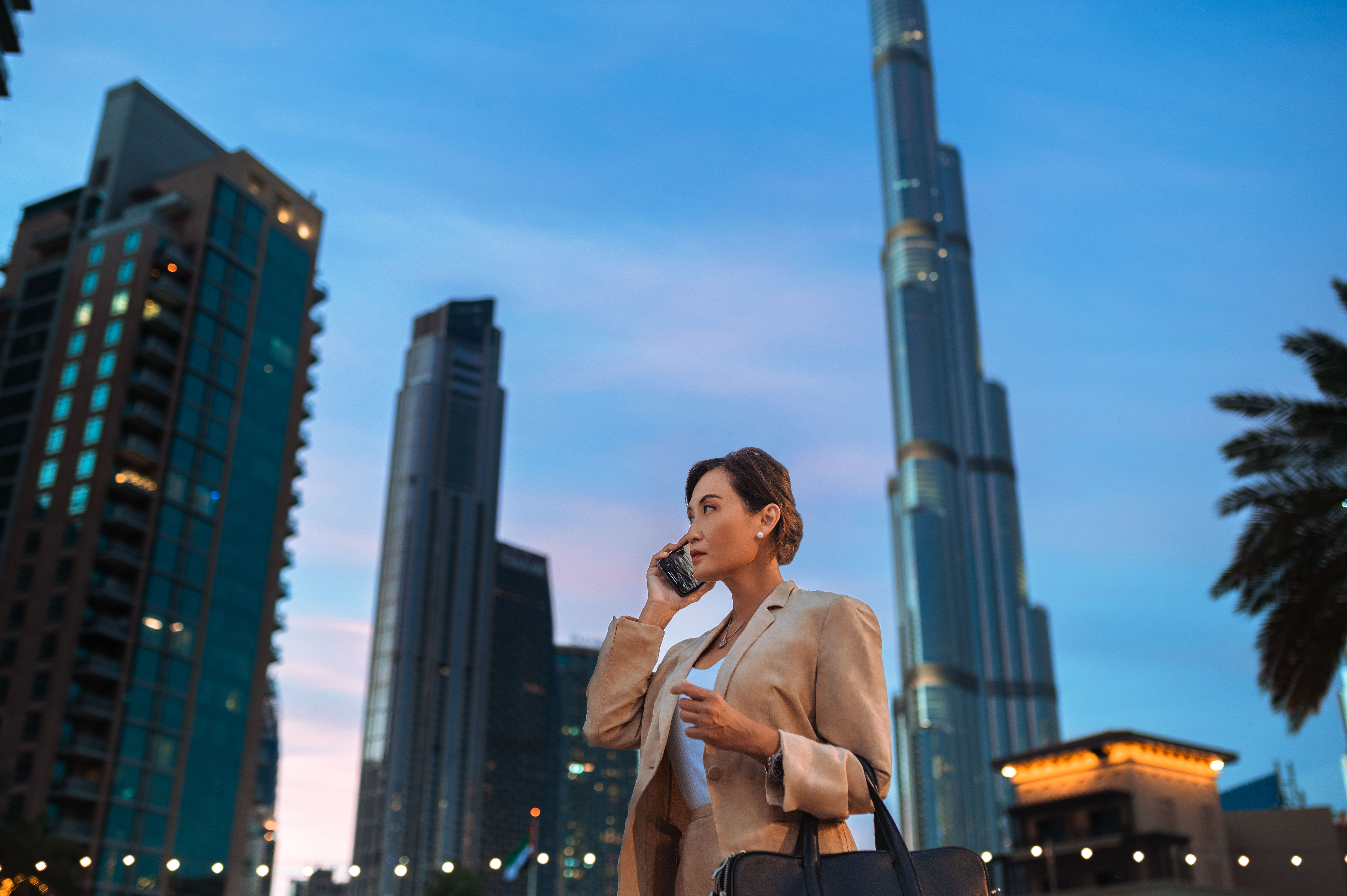 Low angle view of asian businesswoman in beige jacket, listening to conversation with client on cellphone in city center
