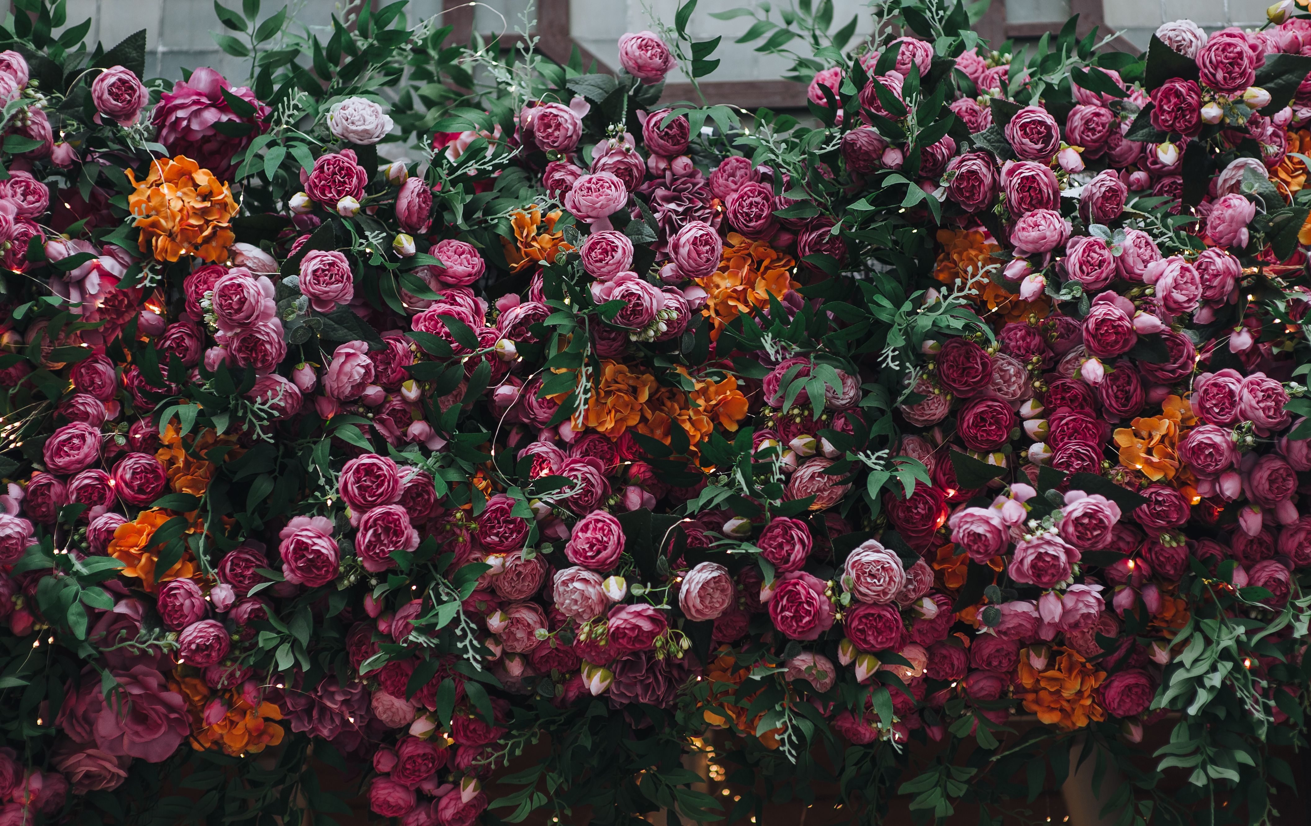 Lots of purple and orange artificial rose flowers and green leaves. Natural background close-up.