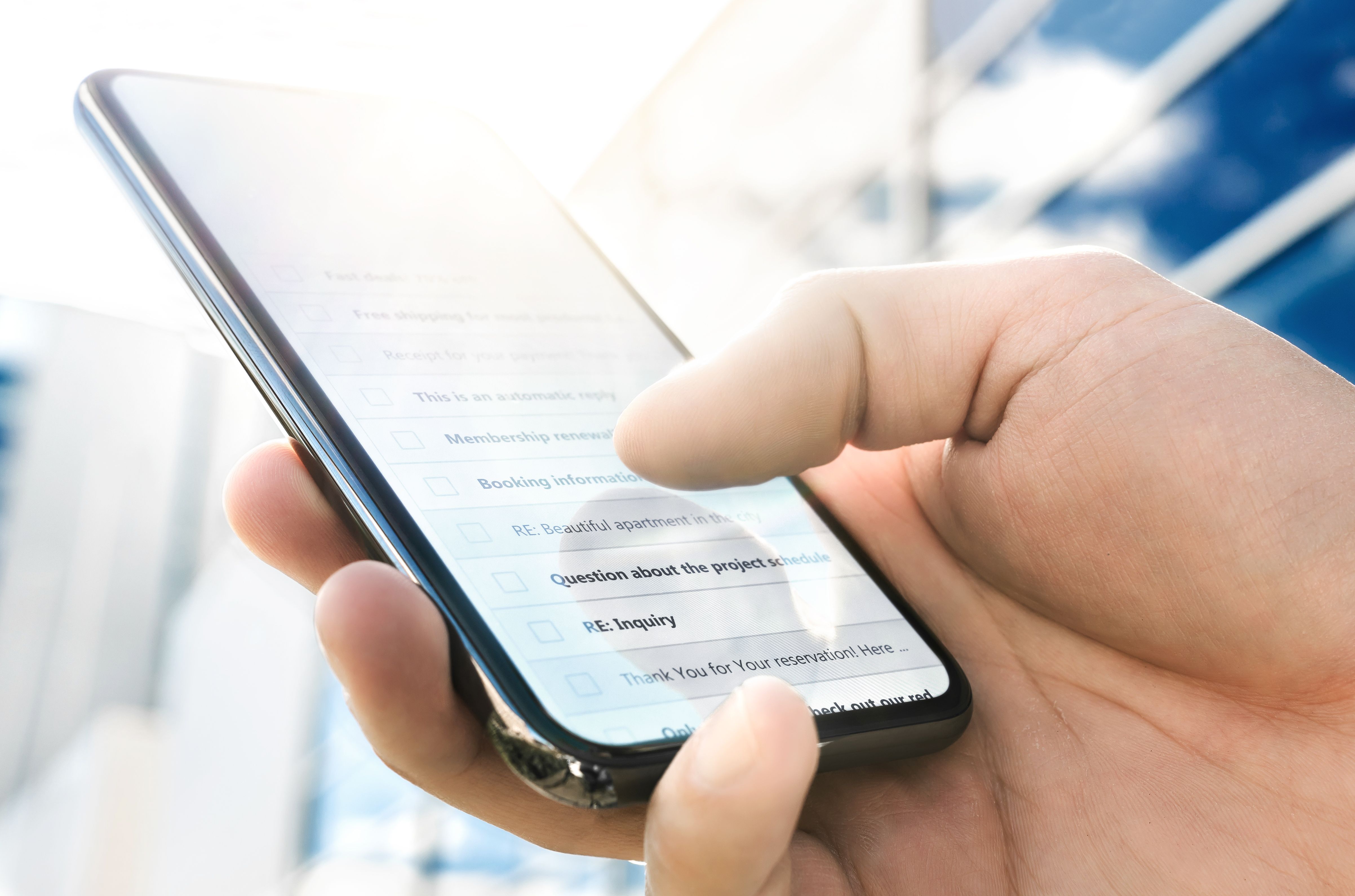 Email inbox with message list in phone. Business man using smartphone outside modern corporate office in urban city on a sunny morning.