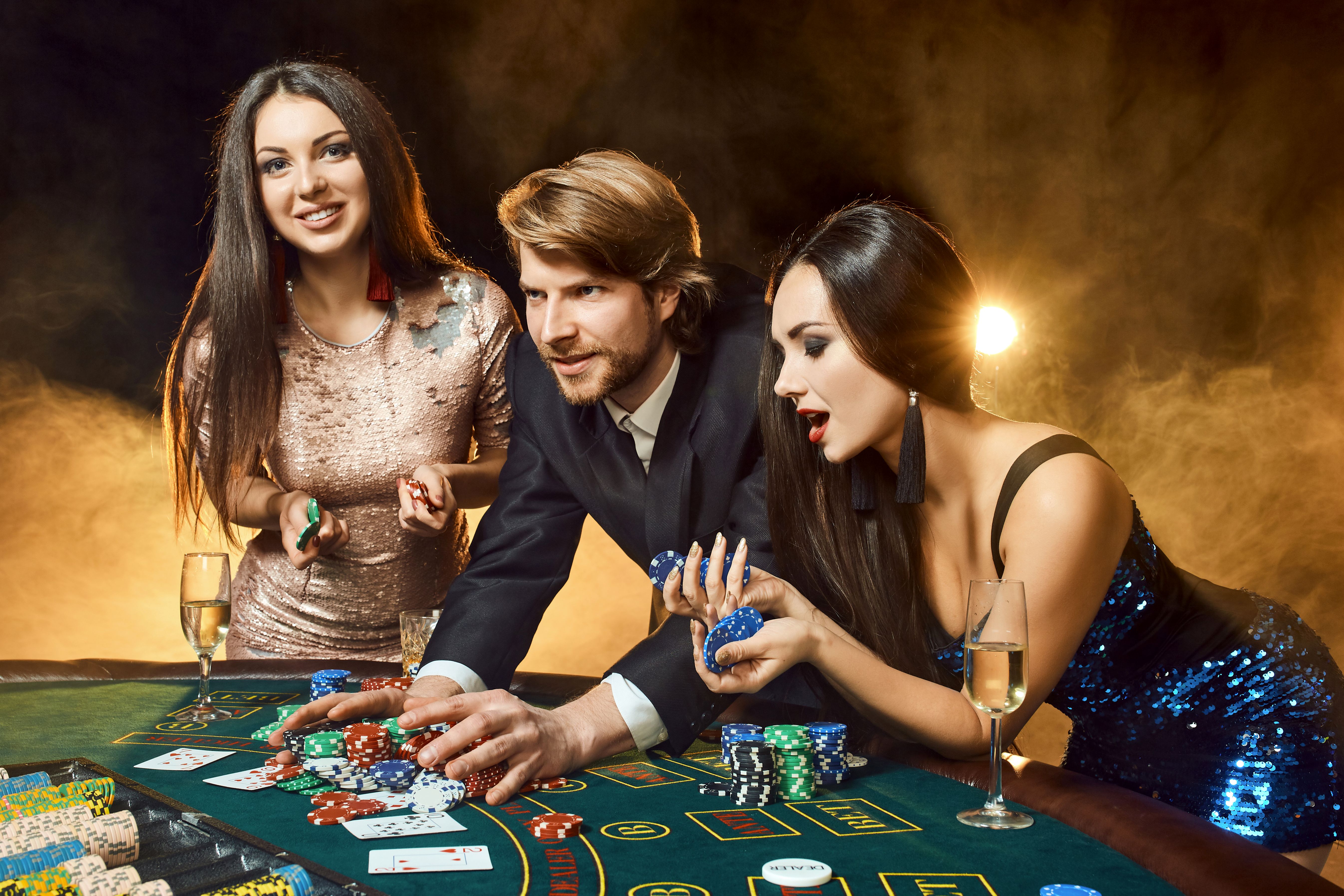 Two beautiful women and young man play on poker table in casino, focus on man and brunette Two beautiful women and young man play on poker table in casino, focus on man and brunette