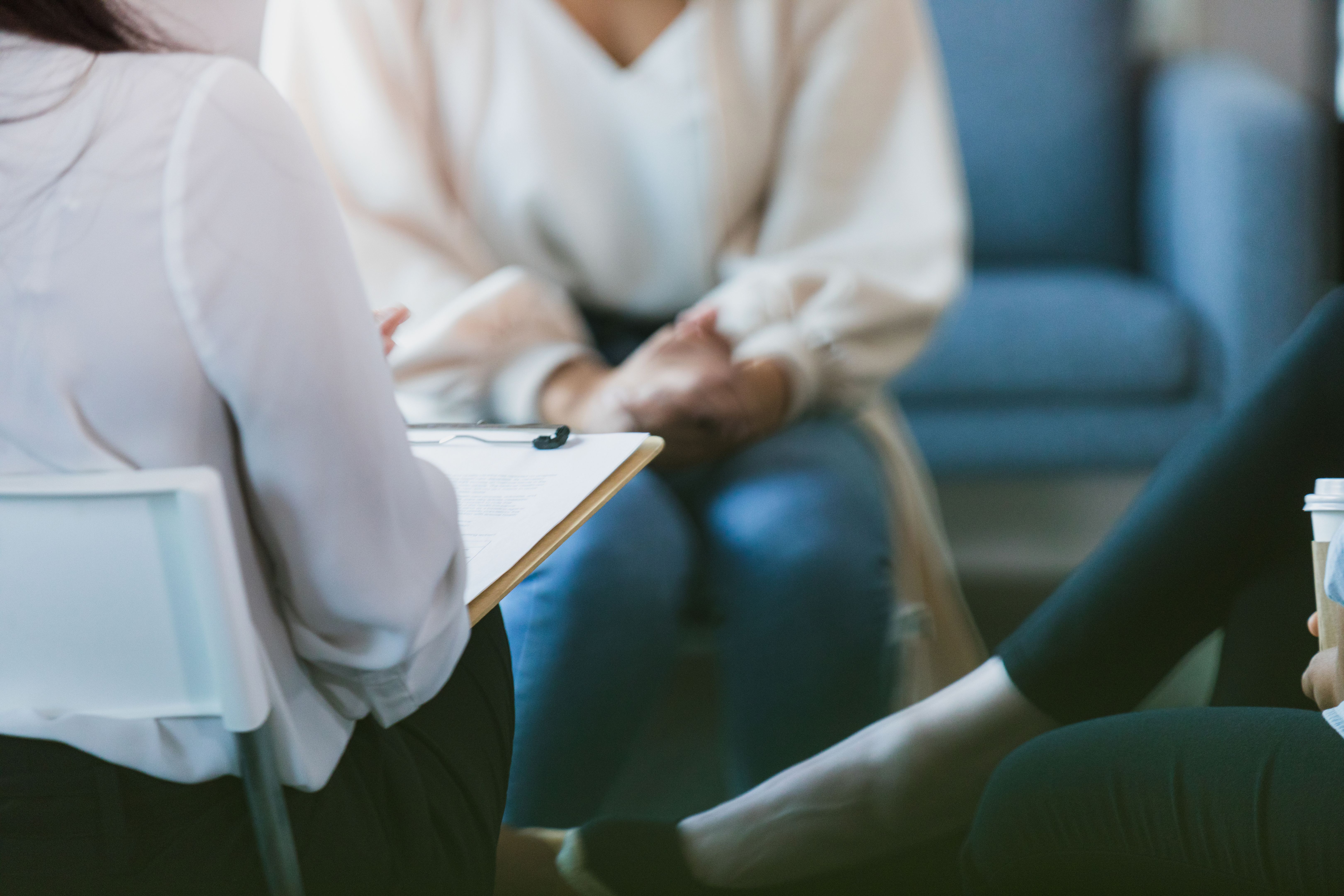 Women in group therapy listen to unrecognizable therapist with clipboard