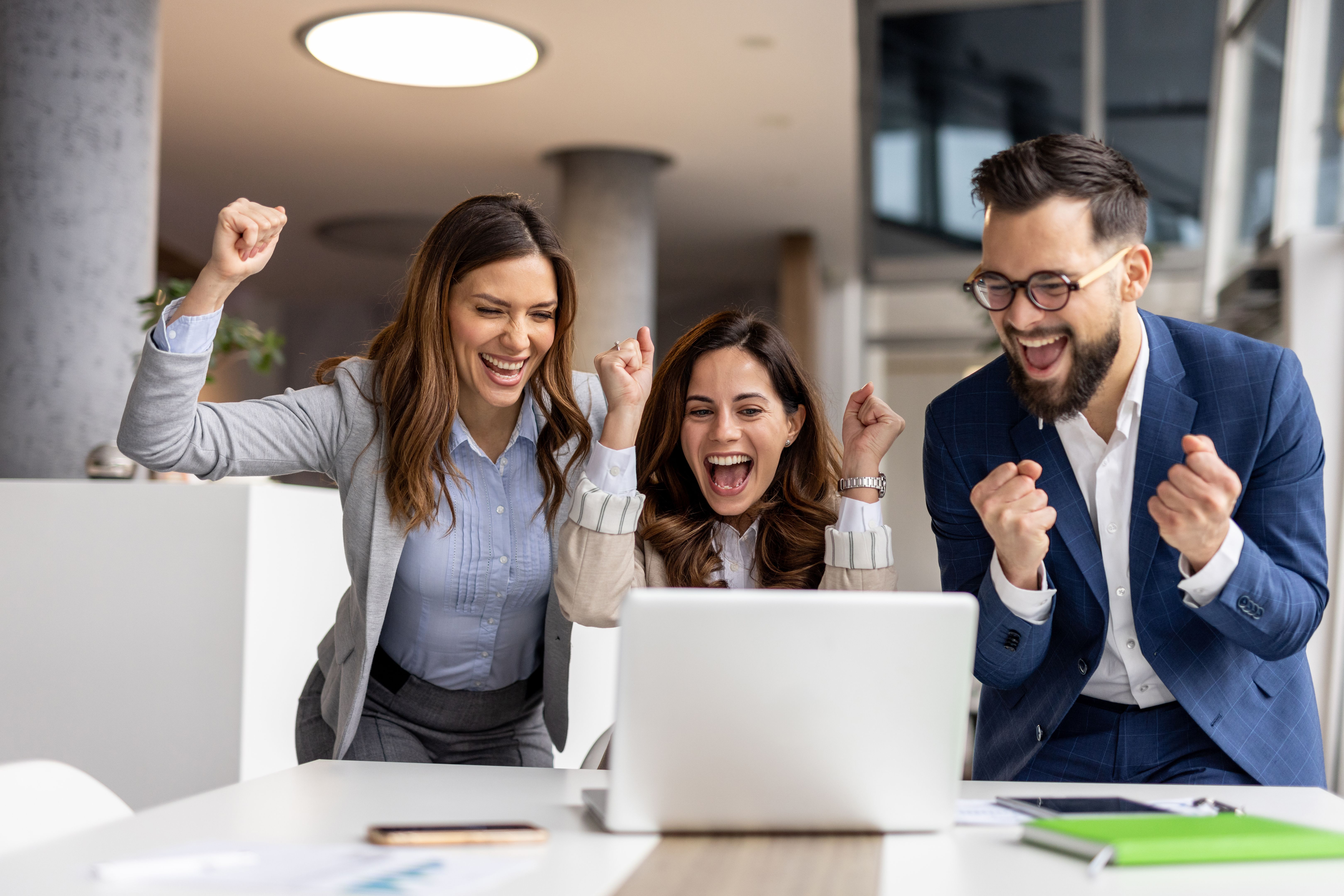 Excited business team celebrating success while looking at laptop in office Excited business team celebrating success while looking at laptop in office
