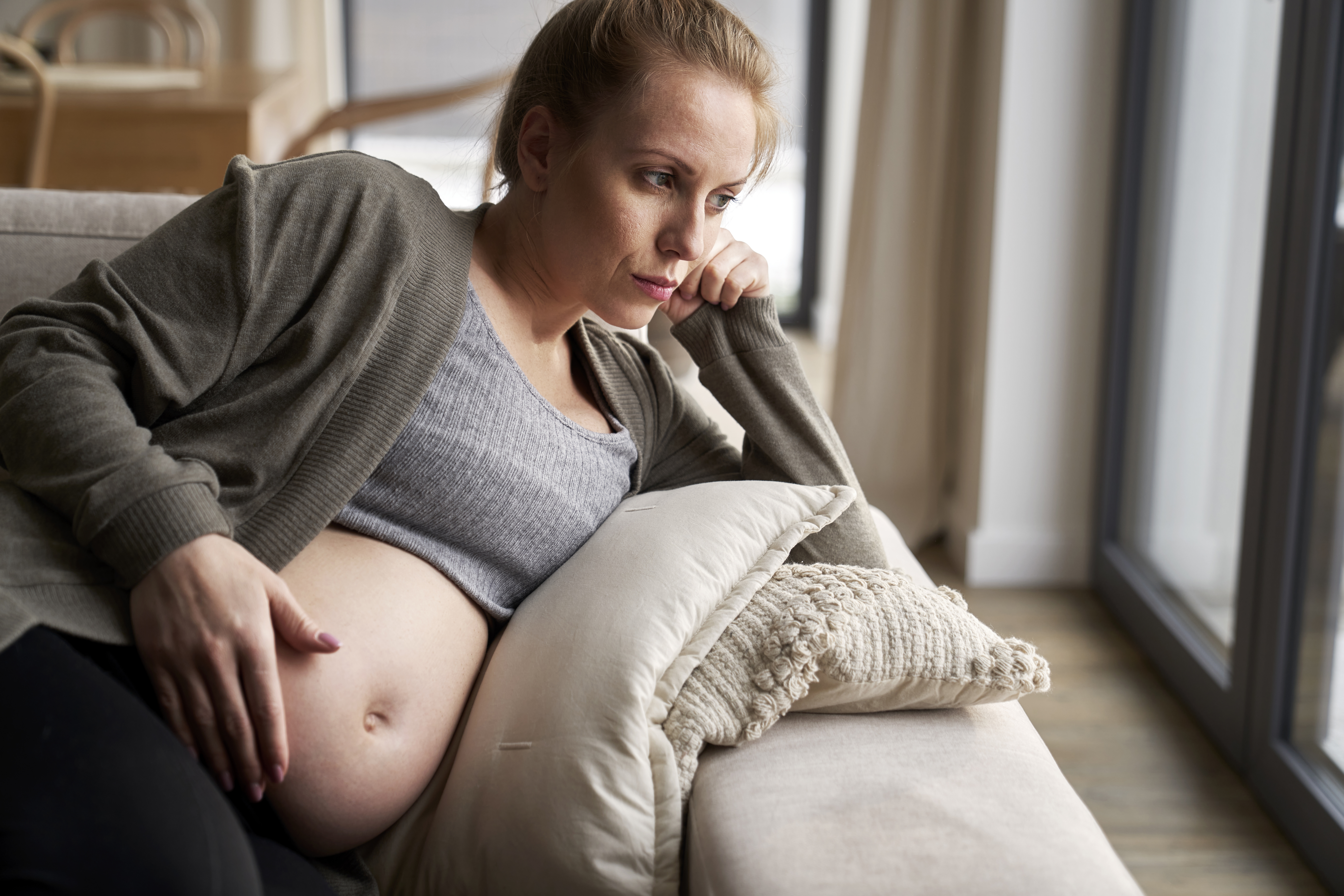 Anxious pregnant woman lying on sofa and touching her abdomen