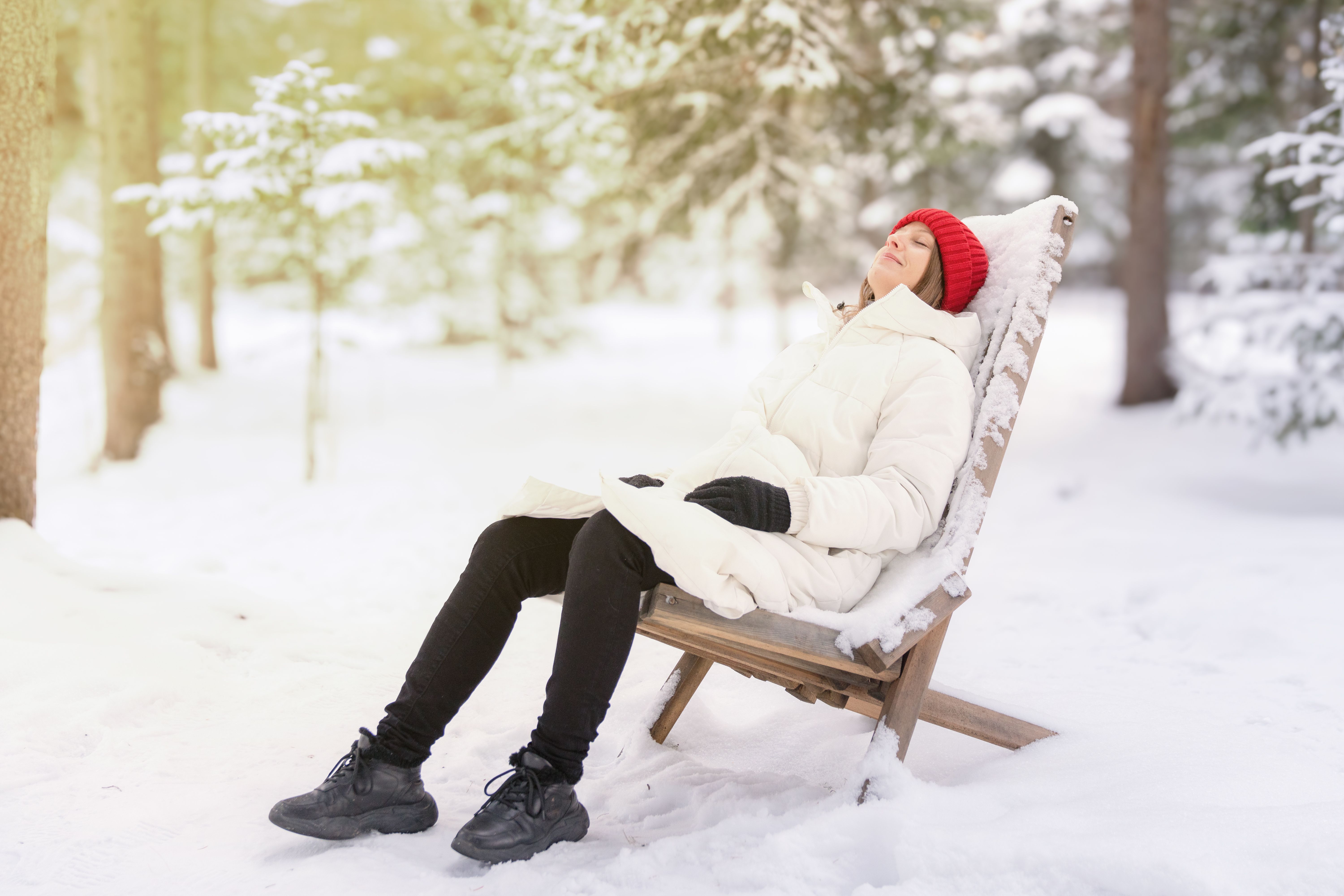 A woman in a white down jacket sits reclining on a wooden armchair in a snowy forest. Relaxing in nature after the Christmas holidays A woman in a white down jacket sits reclining on a wooden armchair in a snowy forest. Relaxing in nature after the Christmas holidays