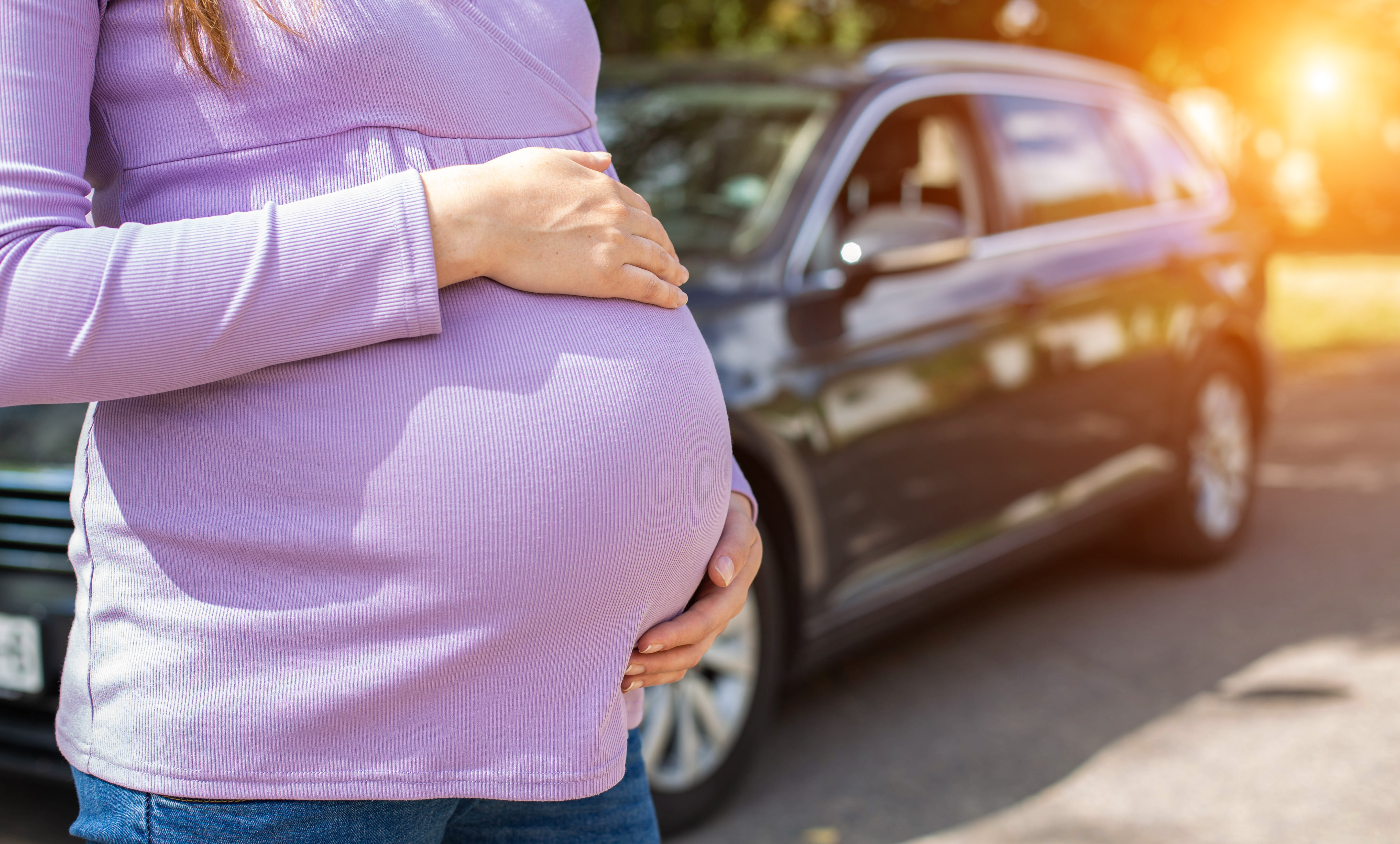 A pregnant girl with a big belly in a purple sweater on the background of a car. The concept of travel and a long trip in a car during pregnancy. Copy space for text A pregnant girl with a big belly in a purple sweater on the background of a car. The concept of travel and a long trip in a car during pregnancy. Copy space for text