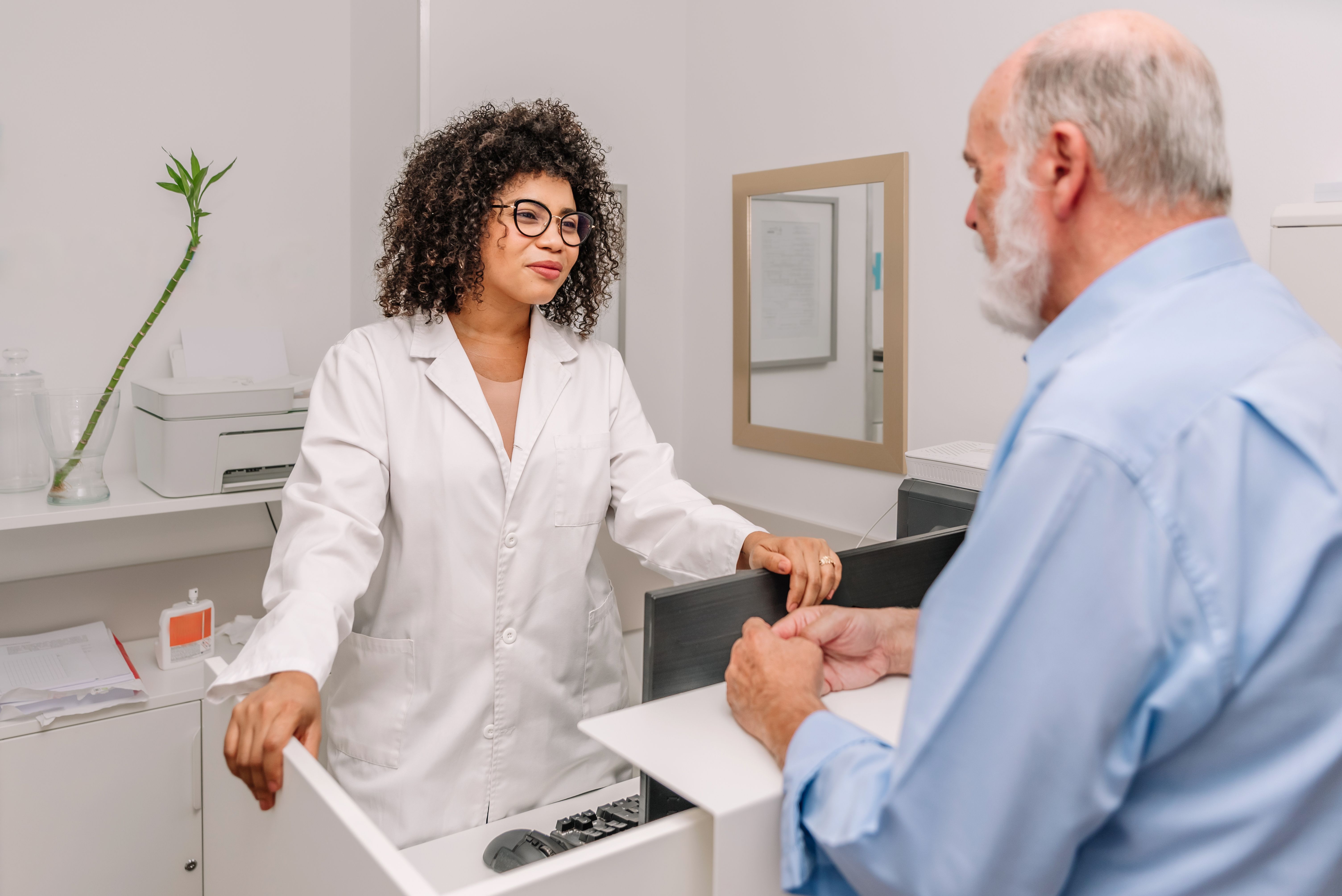 Female Hispanic doctor assisting senior patient at clinic reception desk