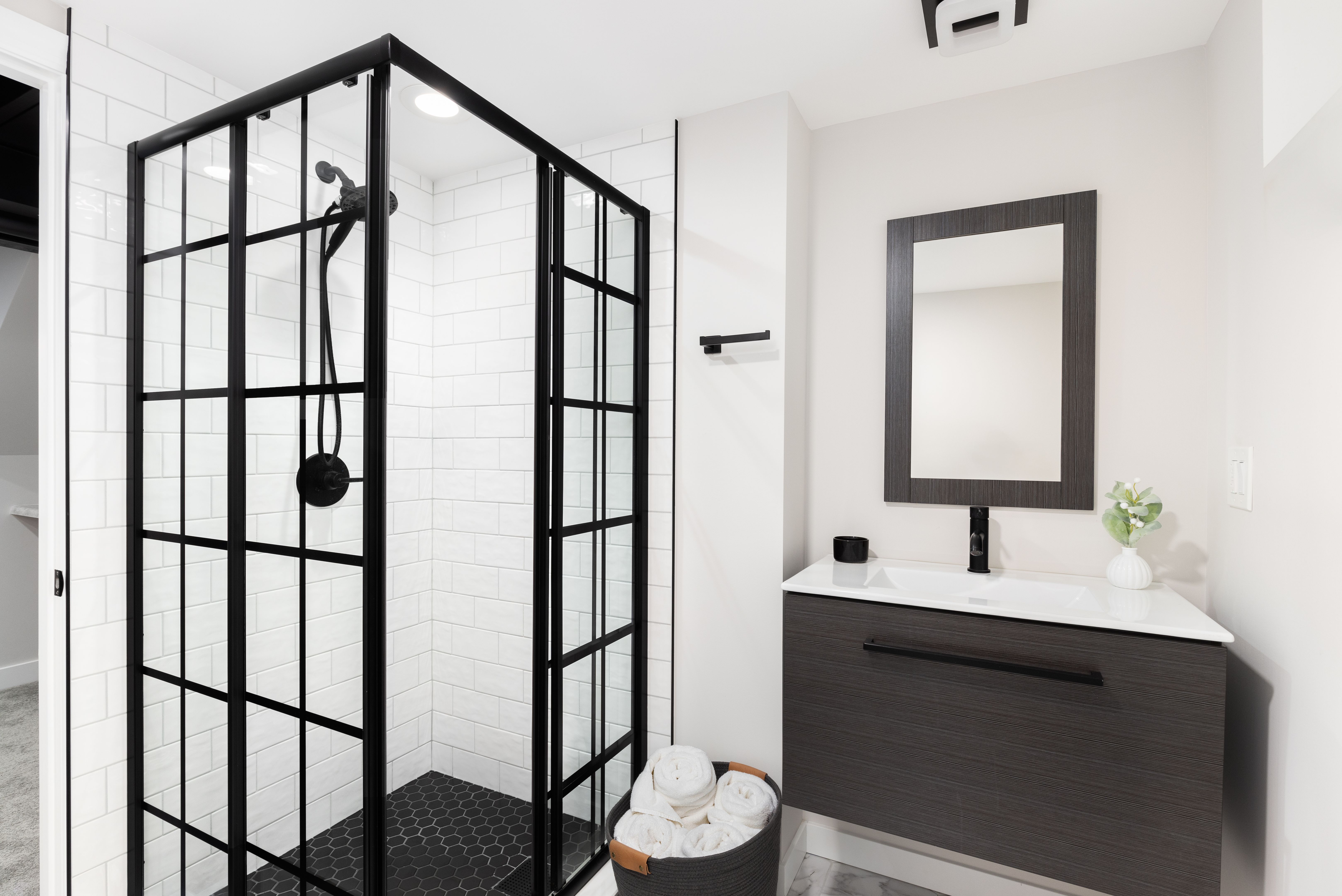 A bathroom with a wood cabinet and a shower with white subway and black hexagon tiles.