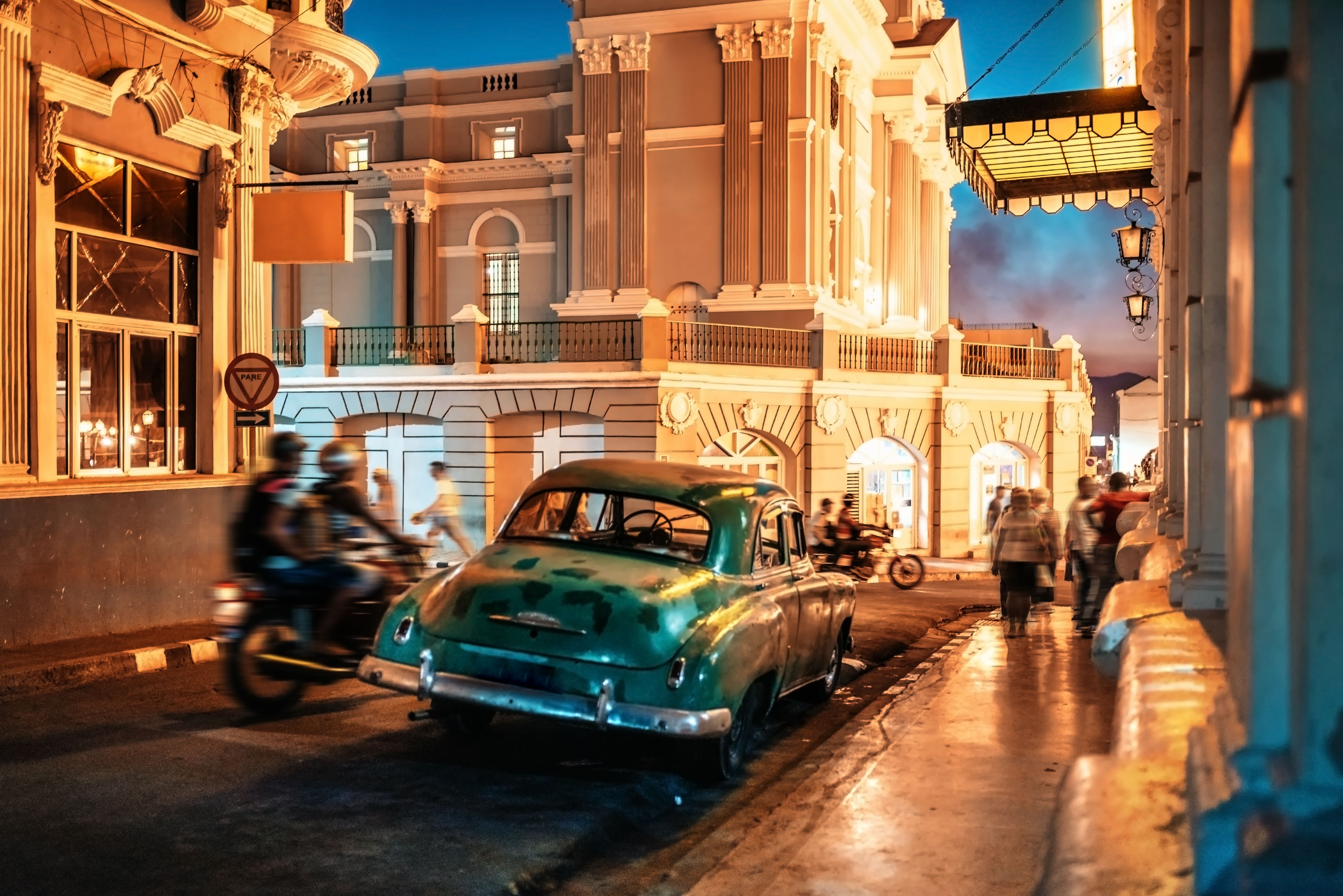 Impression of night streetlife in Santiago de Cuba with old car and people Impression of night streetlife in Santiago de Cuba with old car and people
