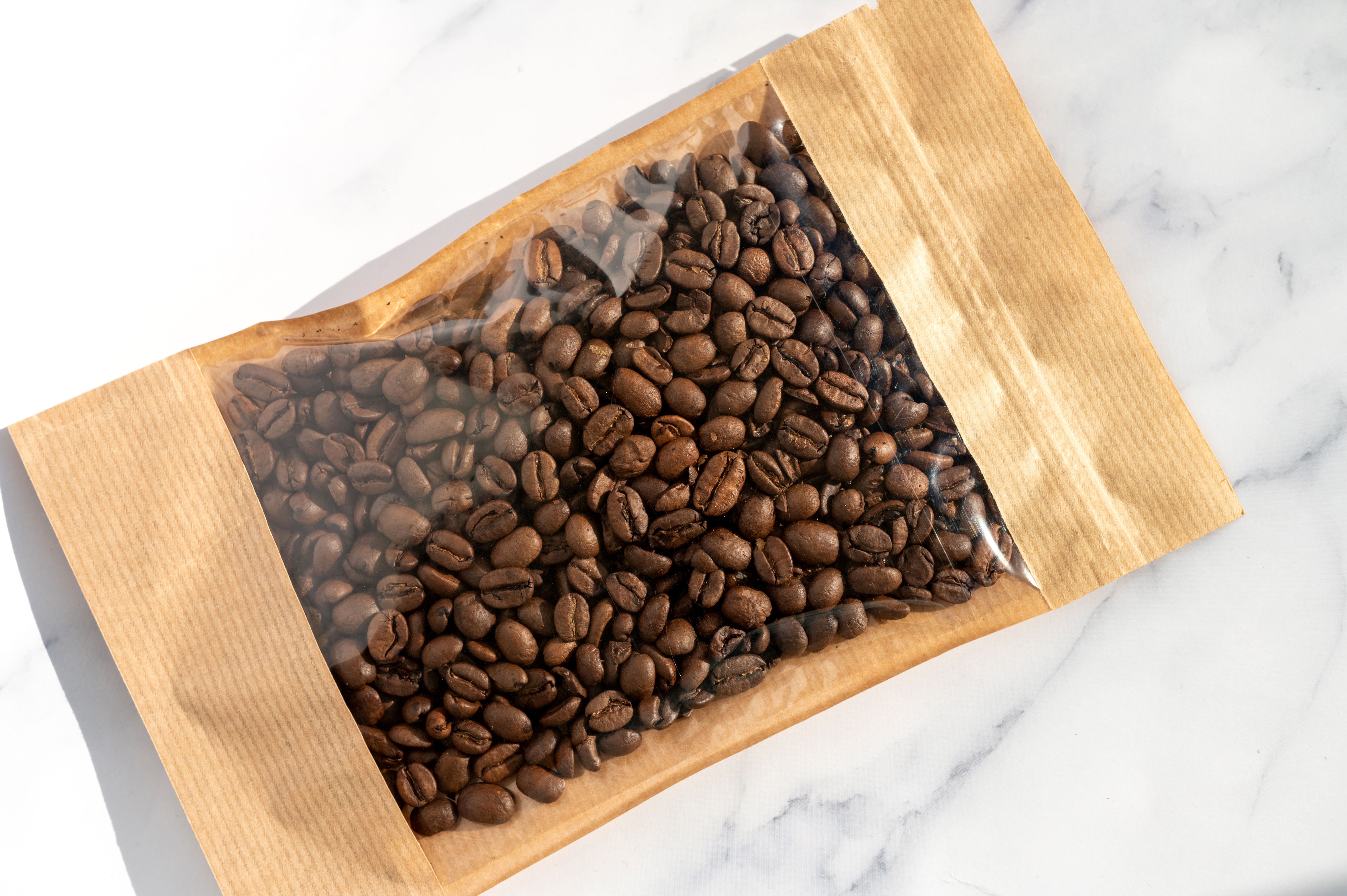 Coffee beans in transparent window pouches on brown paper bags. Coffee beans in transparent window pouches on brown paper bags.