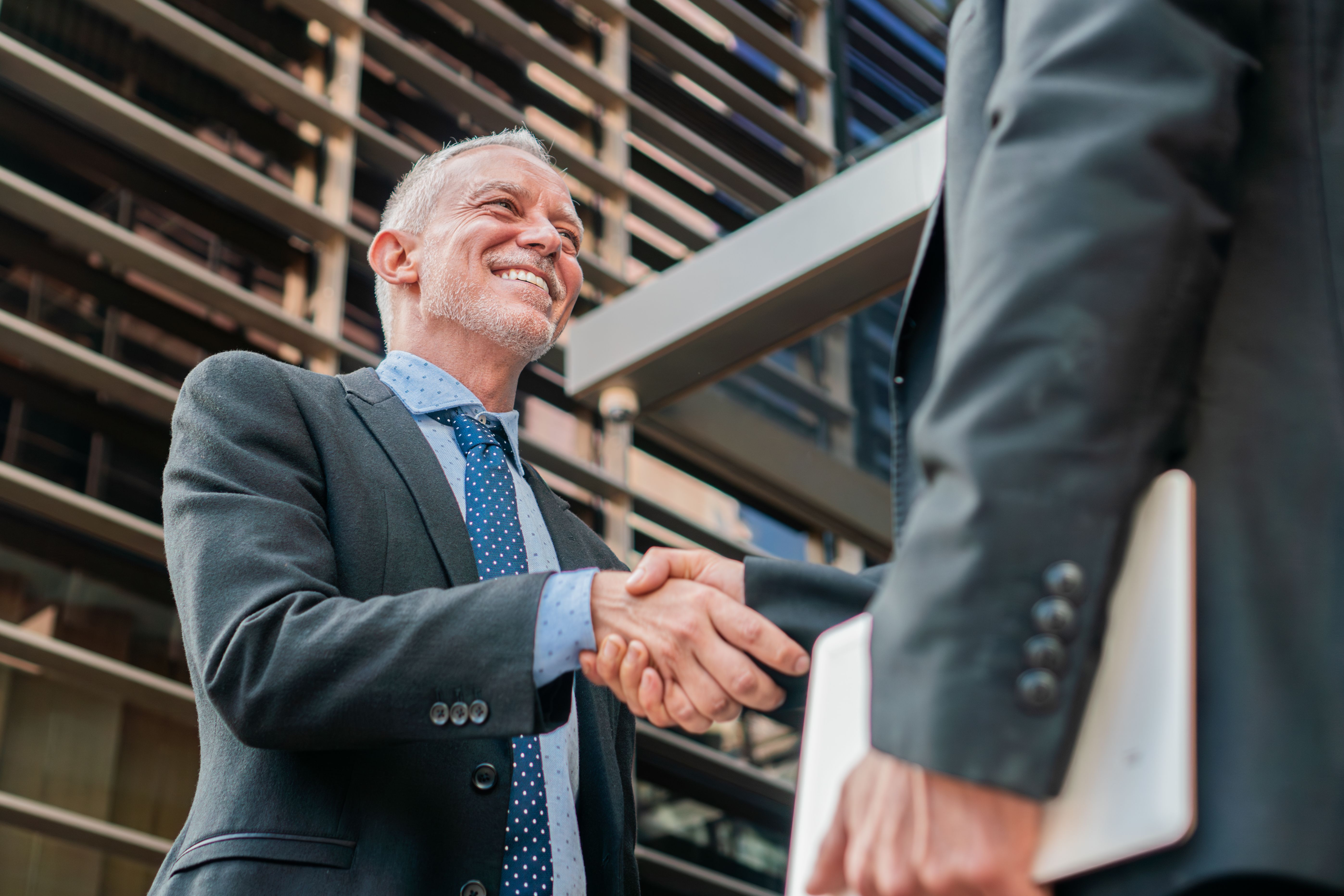Two business men shaking hands for strike a deal. White collar workers smiling and having a collaboration. Businesspeople greeting at workplace. Corporate coworkers or partners in the workspace.