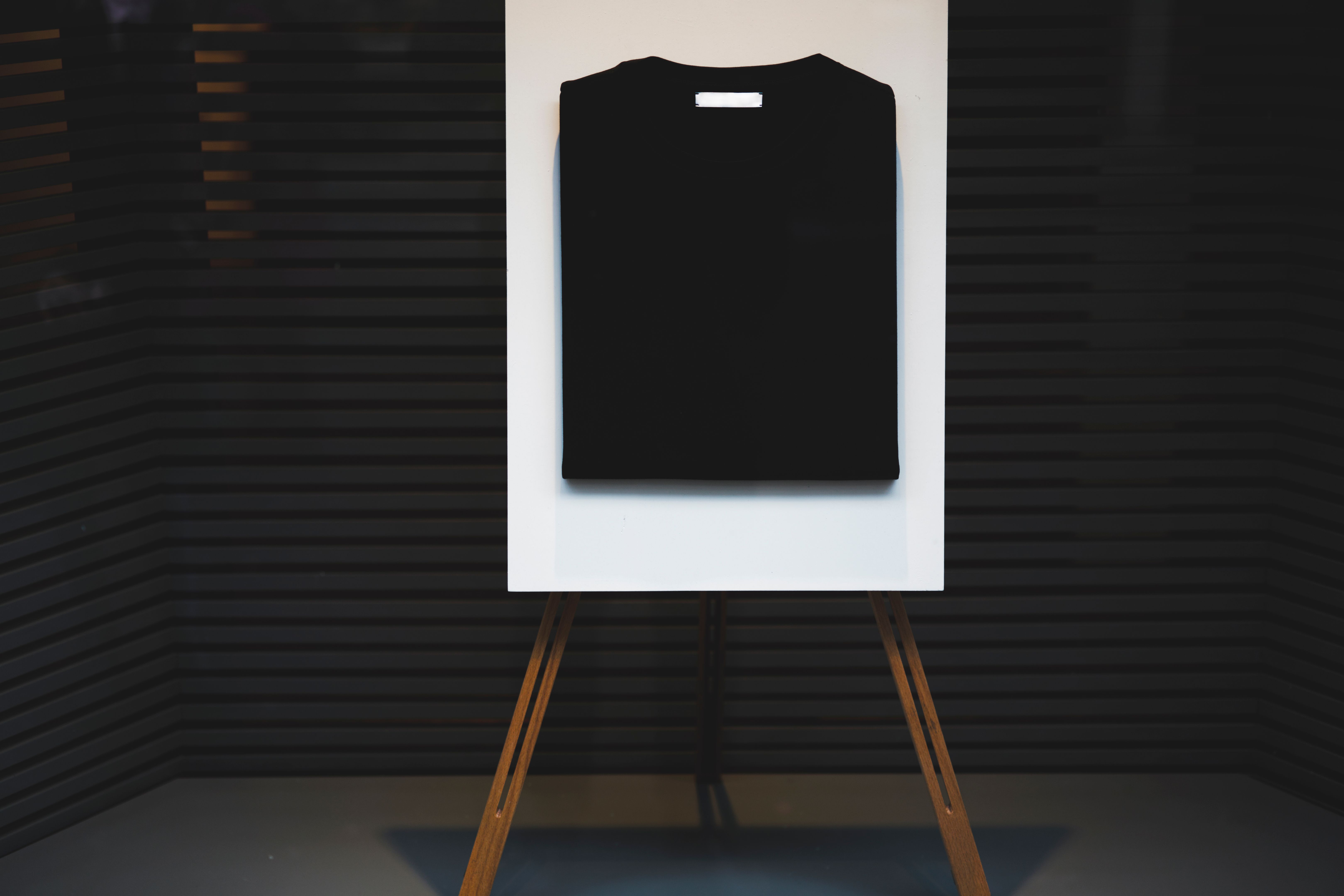 Stylish stand easel with a black basic casual folded t-shirt with mock up copy space area for your logo or brand name, display with clothing at the shop window storefront