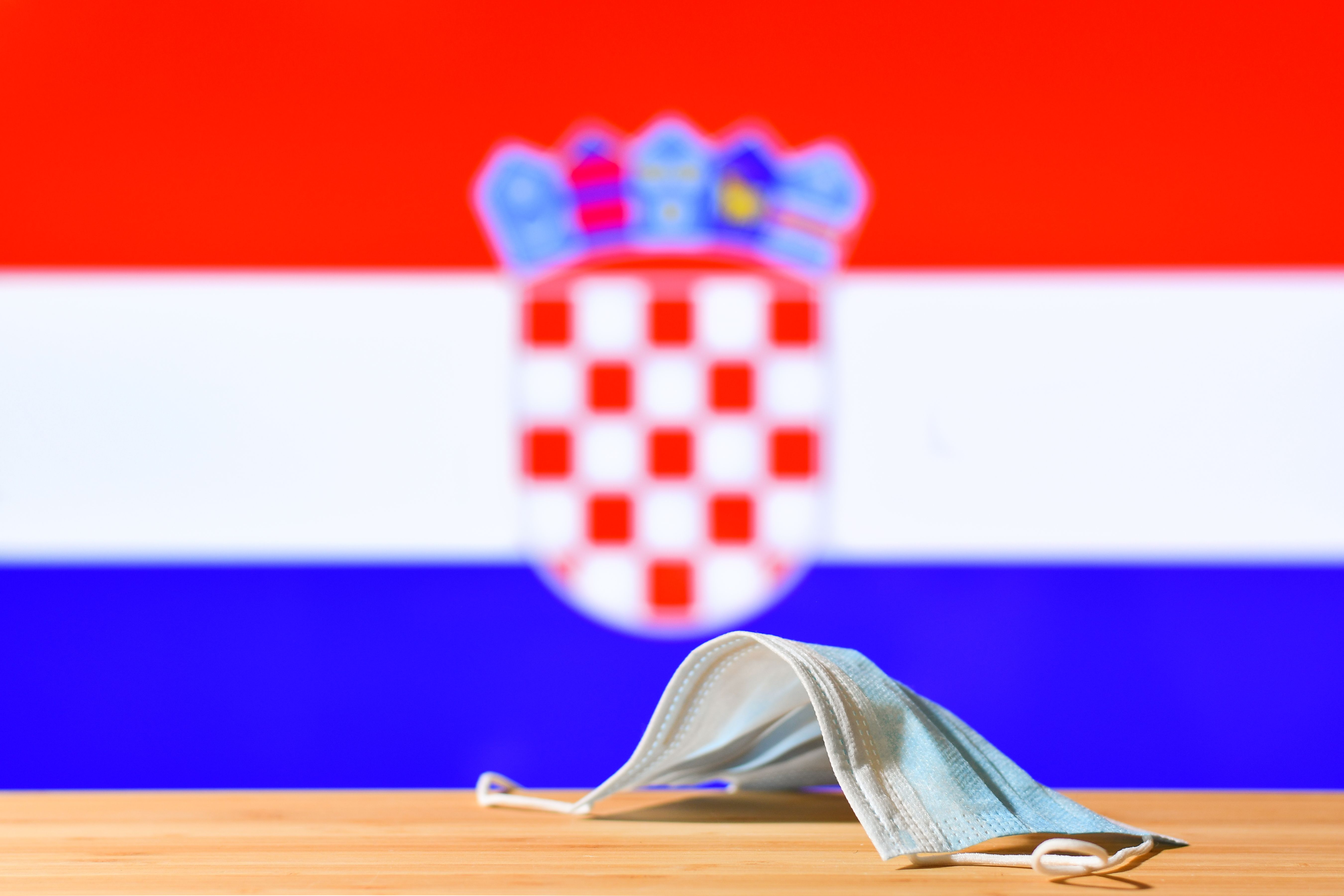 A medical mask lies on the table against the background of the flag of Croatia.