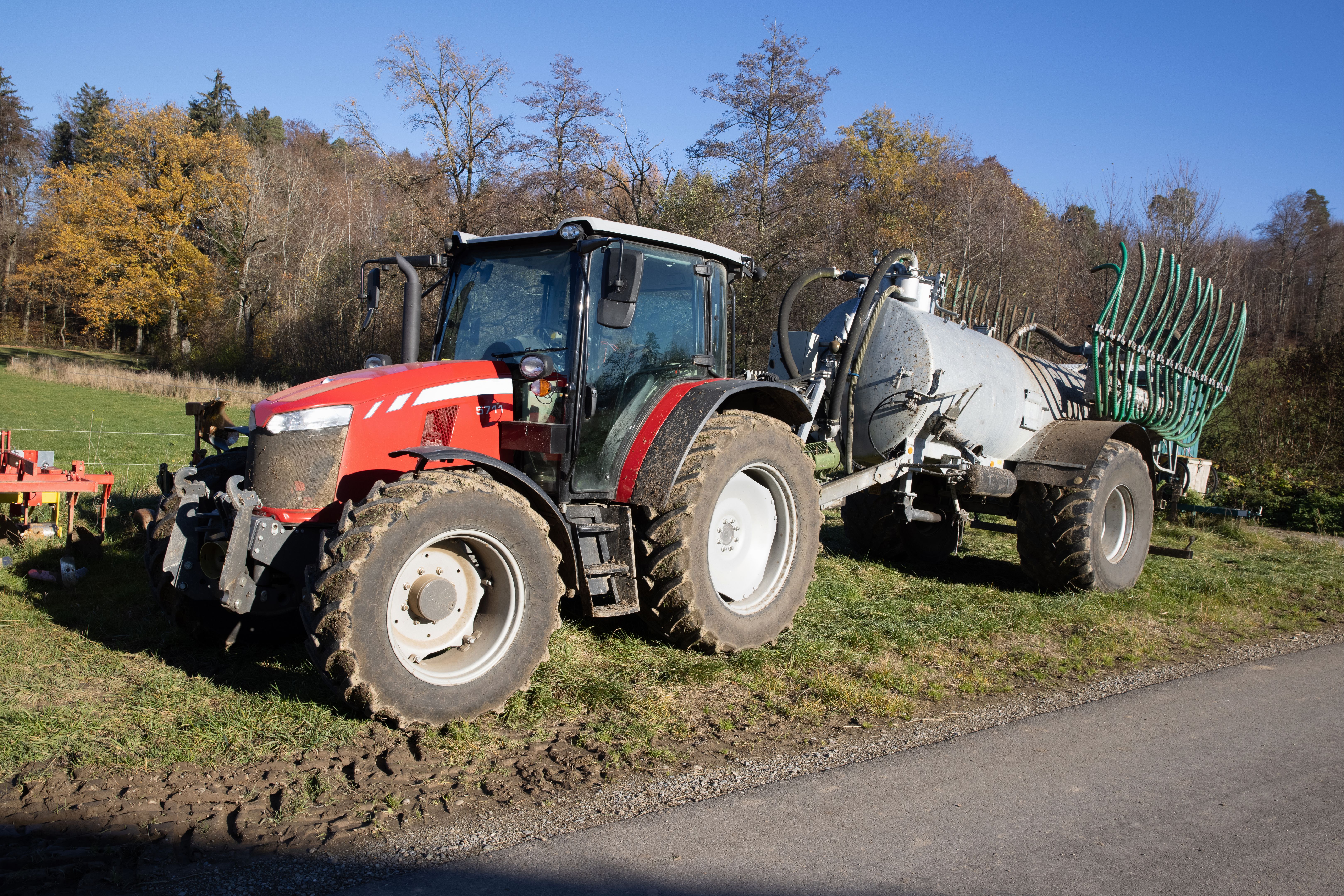 red tractor with slurry tanker and green hoses stands on an autumn meadow, the field can be cultivated faster with these machines, during the day , sunshine without clouds